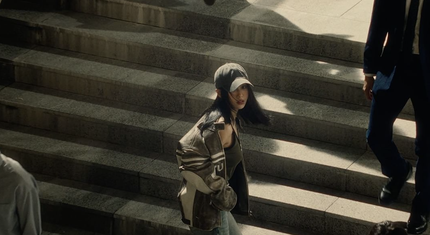Femme marchant sur des escaliers en plein air, portant une casquette et une veste, entourée d'autres personnes.