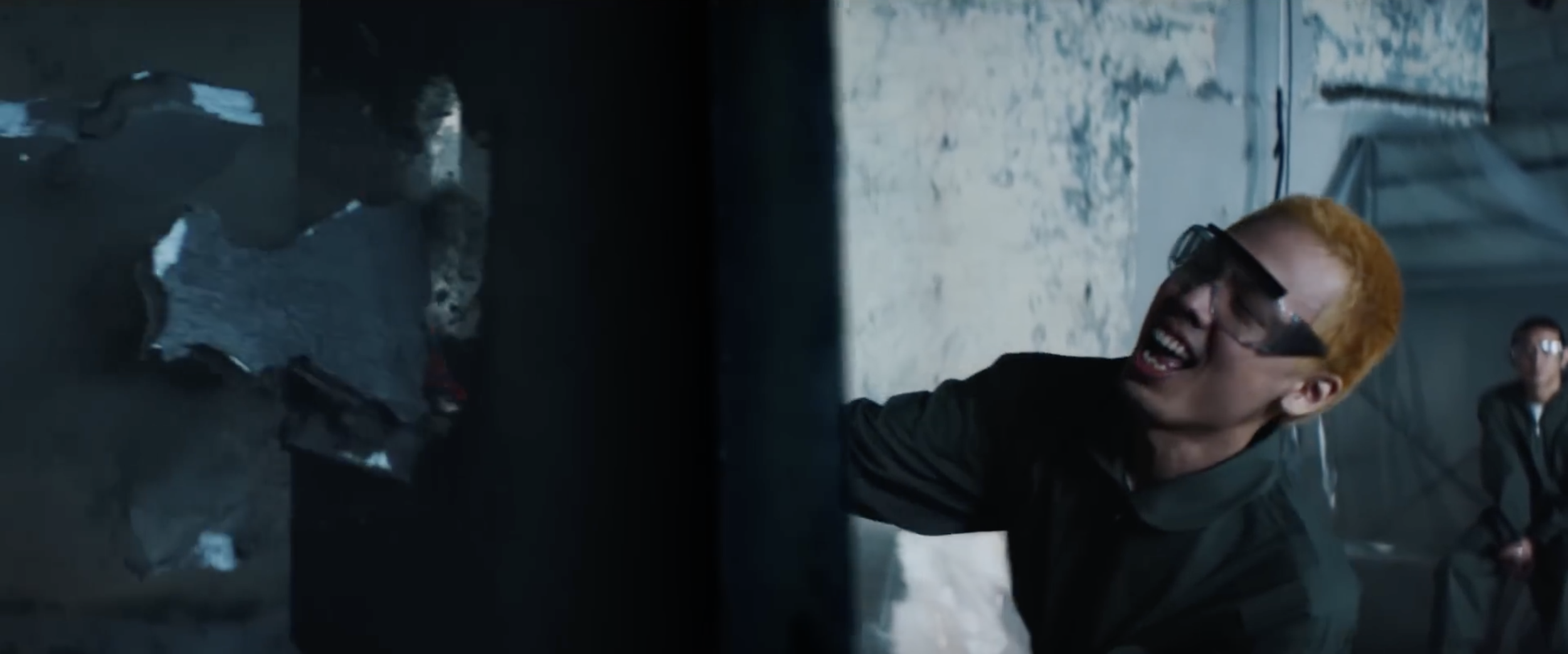 Une personne portant des lunettes de protection pousse une porte métallique abîmée dans un bâtiment industriel.