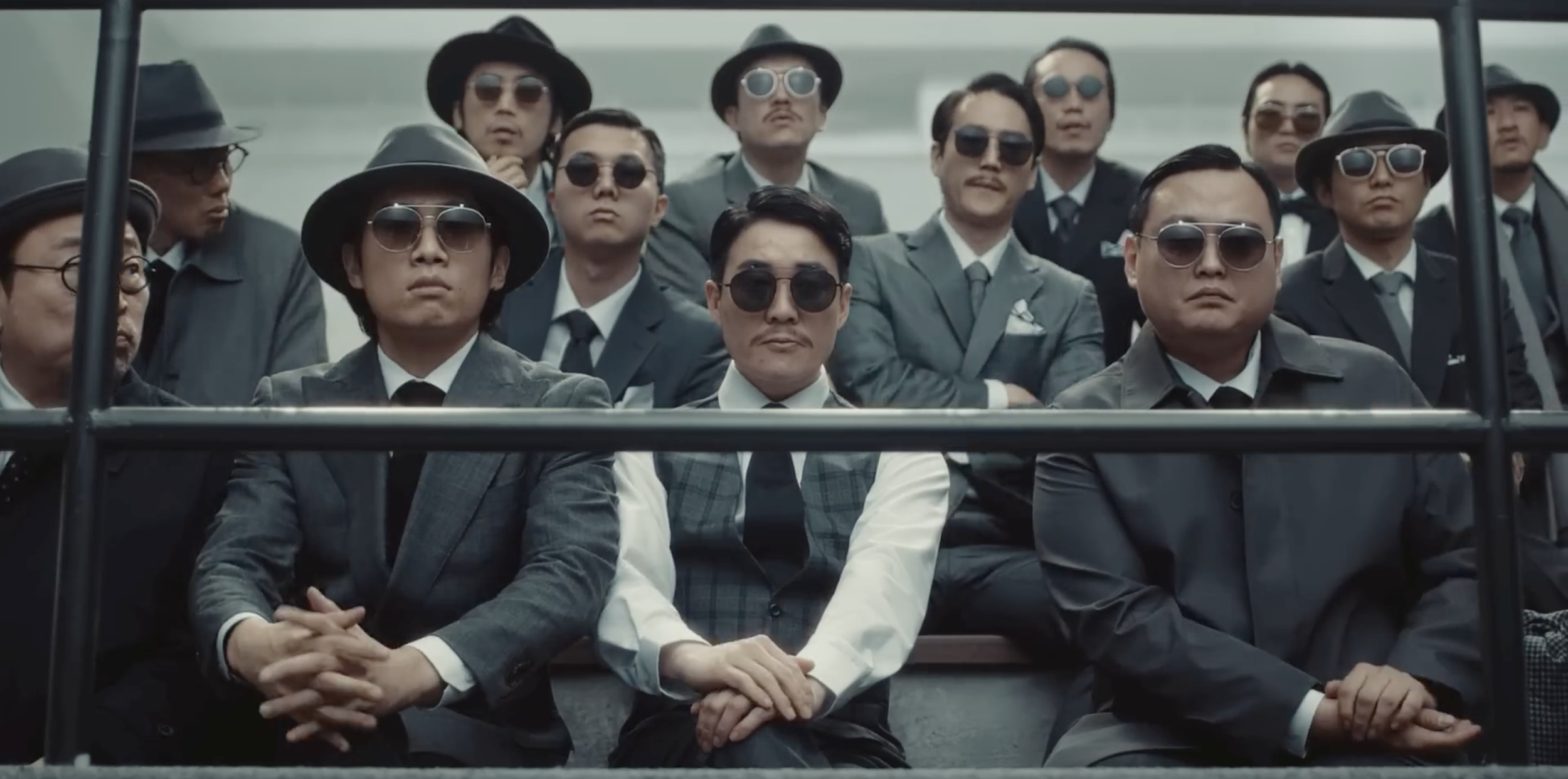 Groupe d'hommes en costumes sombres et lunettes de soleil, assis.