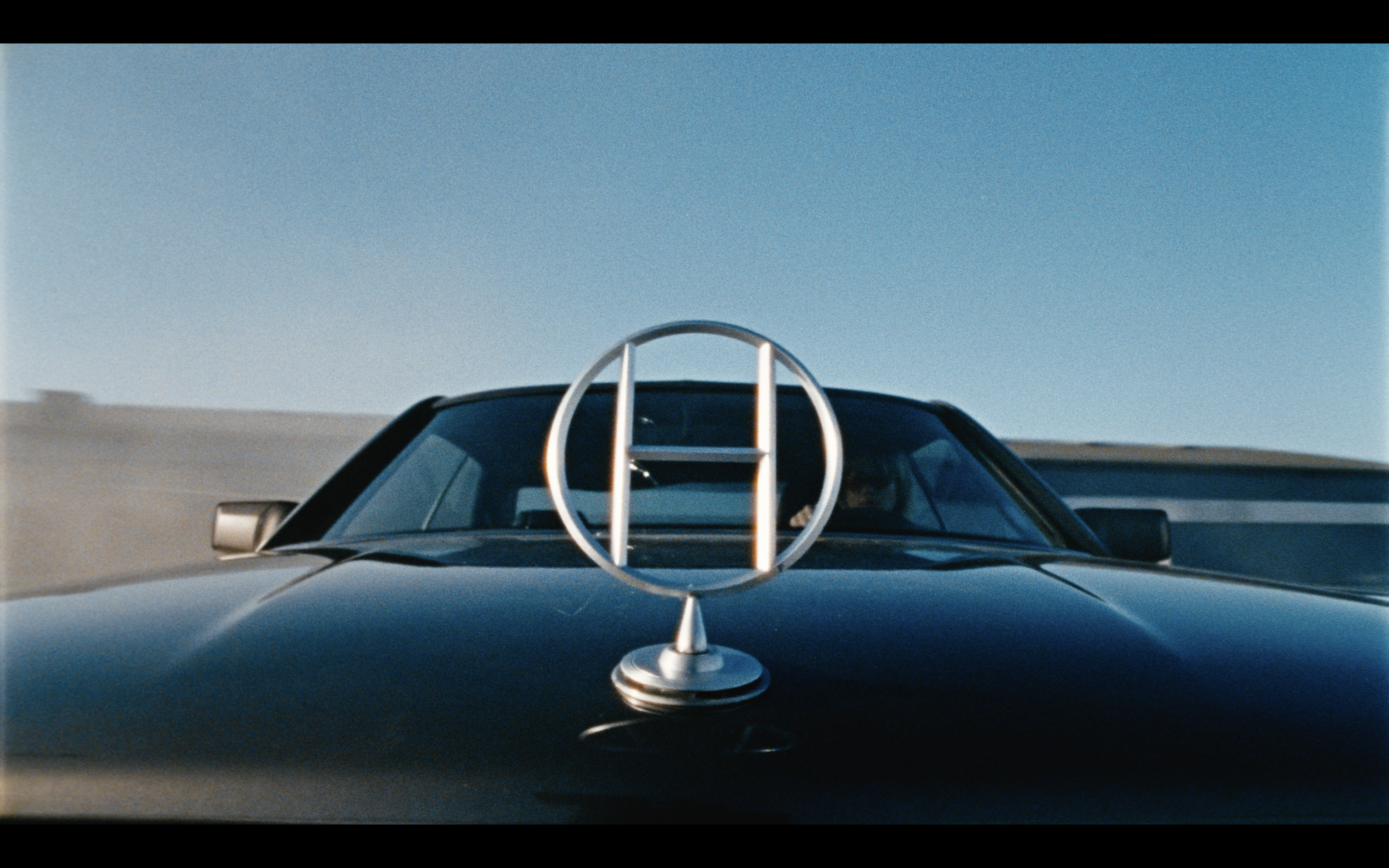 Emblème argenté sur le capot d'une voiture noire sous un ciel bleu.