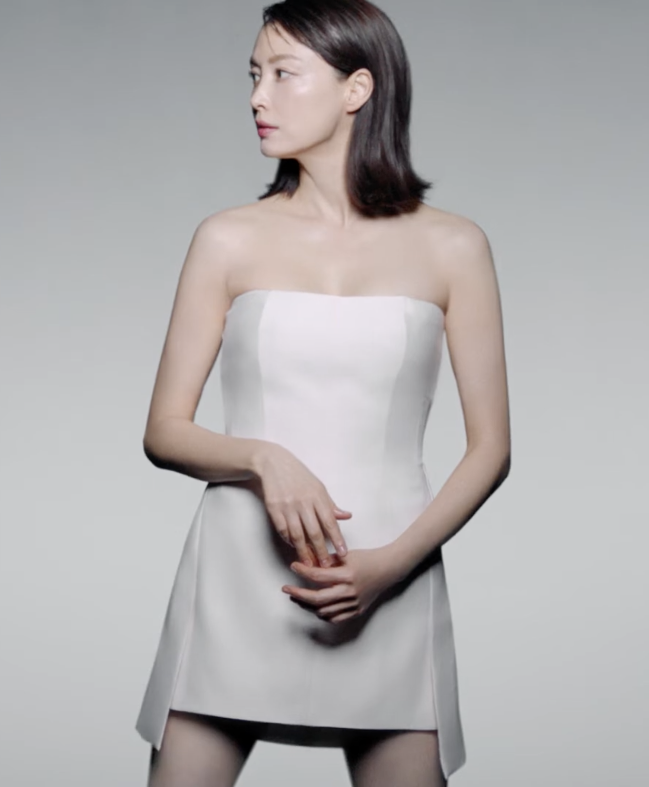 Femme portant une robe blanche sans bretelles, fond gris.