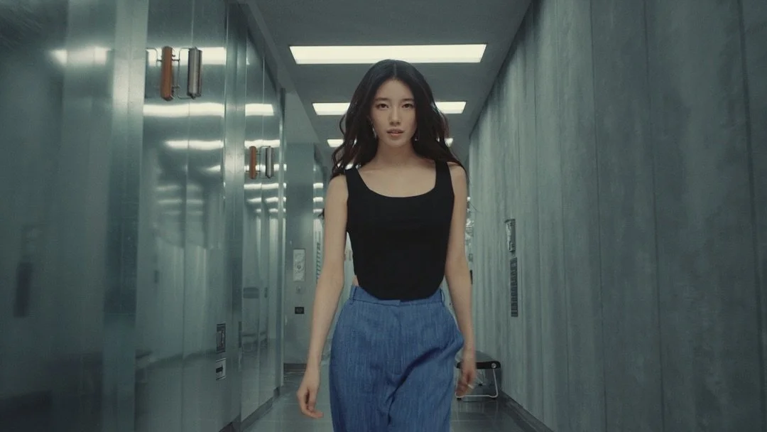 Femme marchant dans un couloir moderne avec des murs métalliques, portant un débardeur noir et un pantalon bleu.