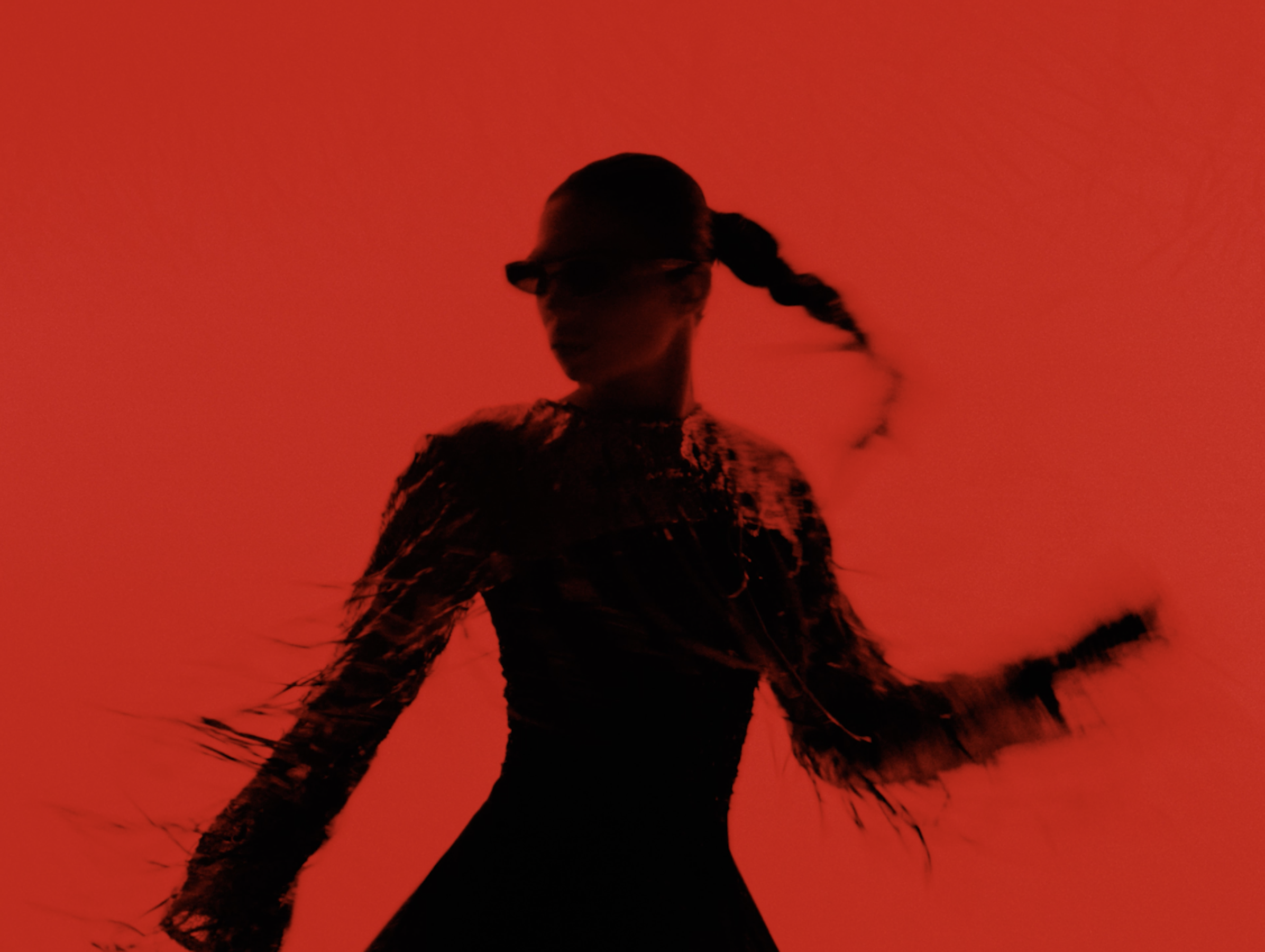Silhouette floue d'une personne en mouvement sur fond rouge, portant des lunettes et une coiffure avec une tresse.
