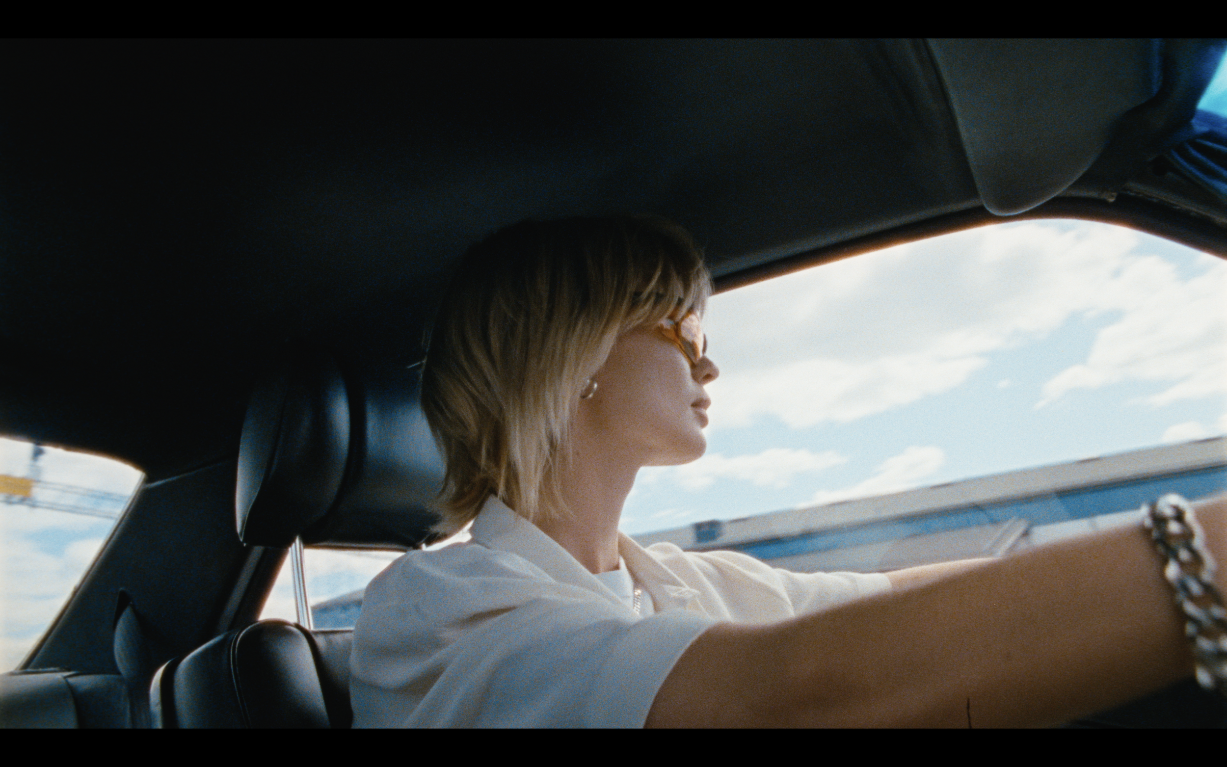 Femme blonde conduisant une voiture, portant des lunettes de soleil.