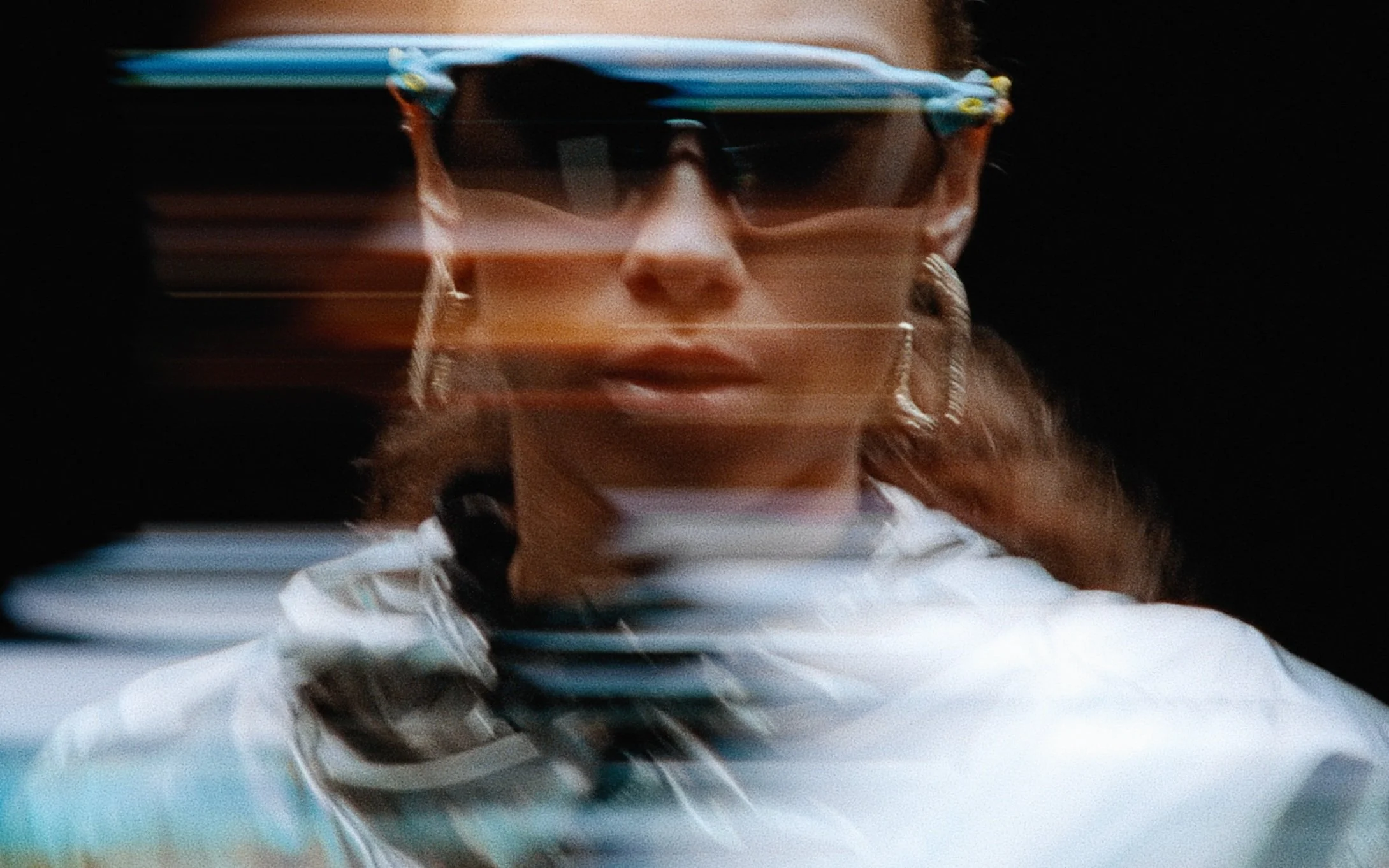 Personne portant des lunettes de soleil et des boucles d'oreilles, image floue avec des effets de mouvement horizontal.