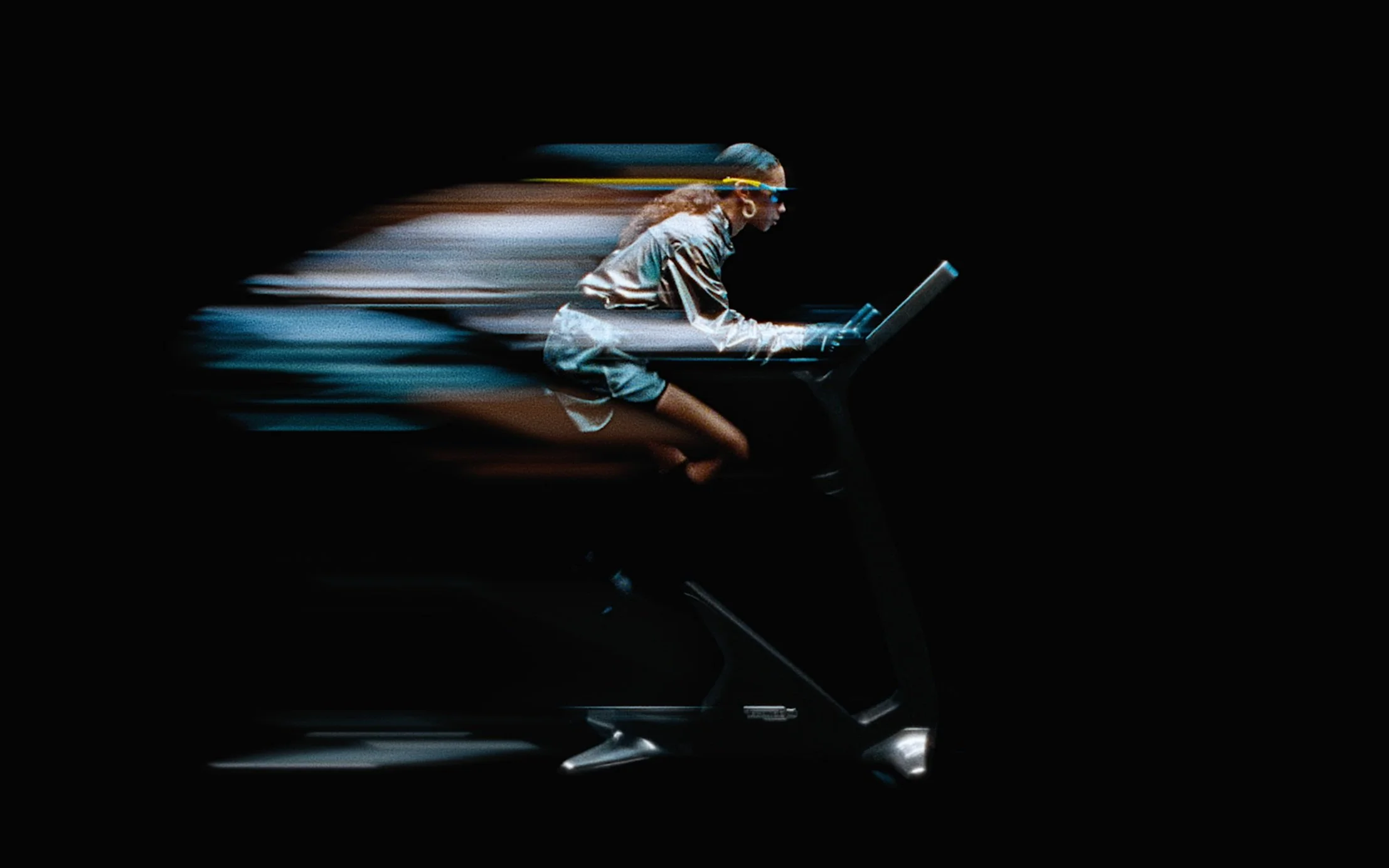 Une personne en mouvement rapide sur un vélo d'intérieur, avec un effet de flou, sur fond noir.