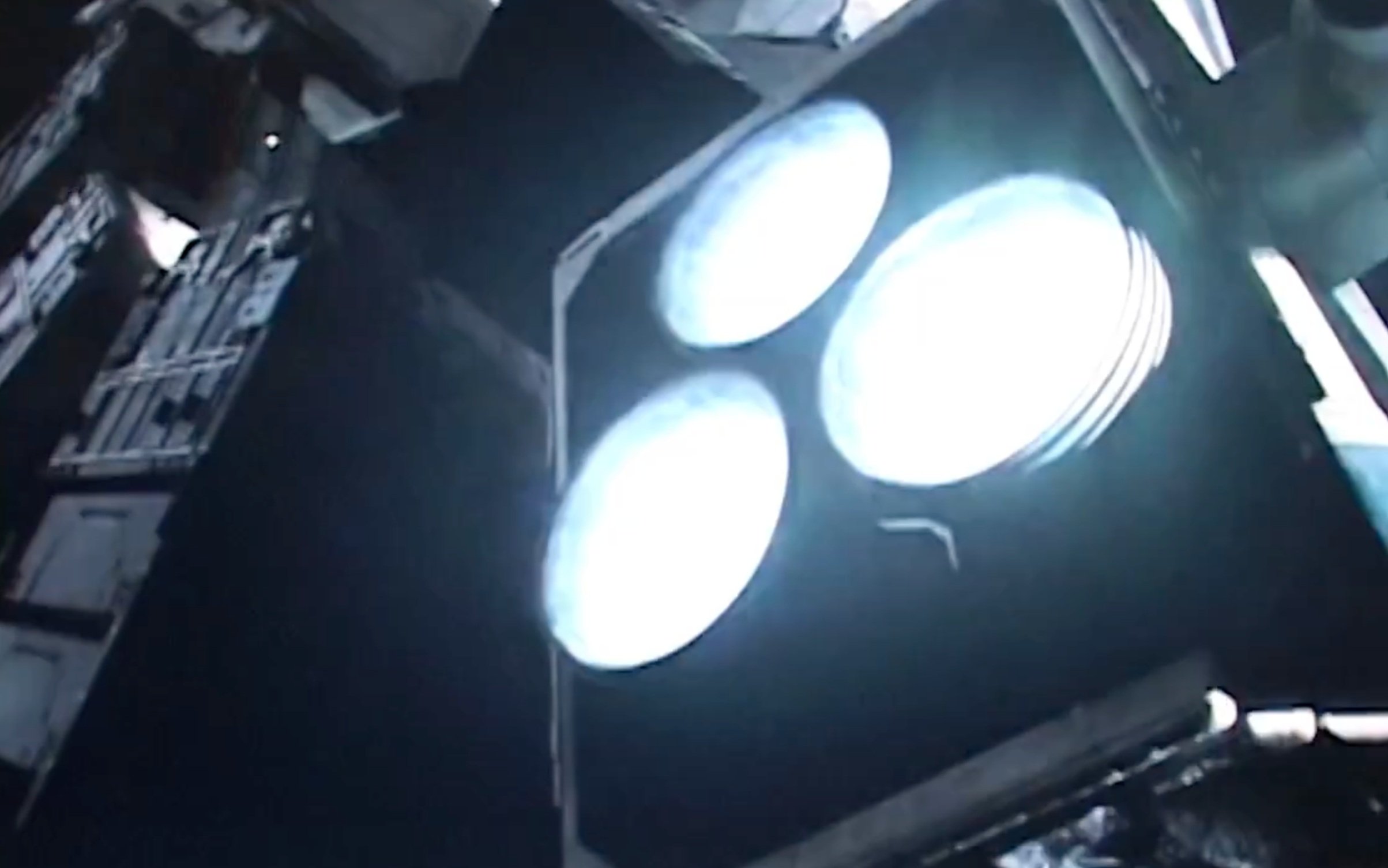 Vue d'une partie d'une station spatiale ou d'un satellite, avec des panneaux et des structures métalliques visibles, éclairés par une lumière intense.