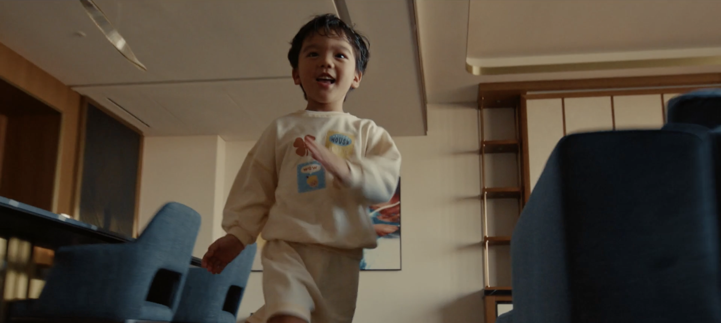 Enfant souriant courant à l'intérieur d'une pièce, portant un pull à motifs colorés.