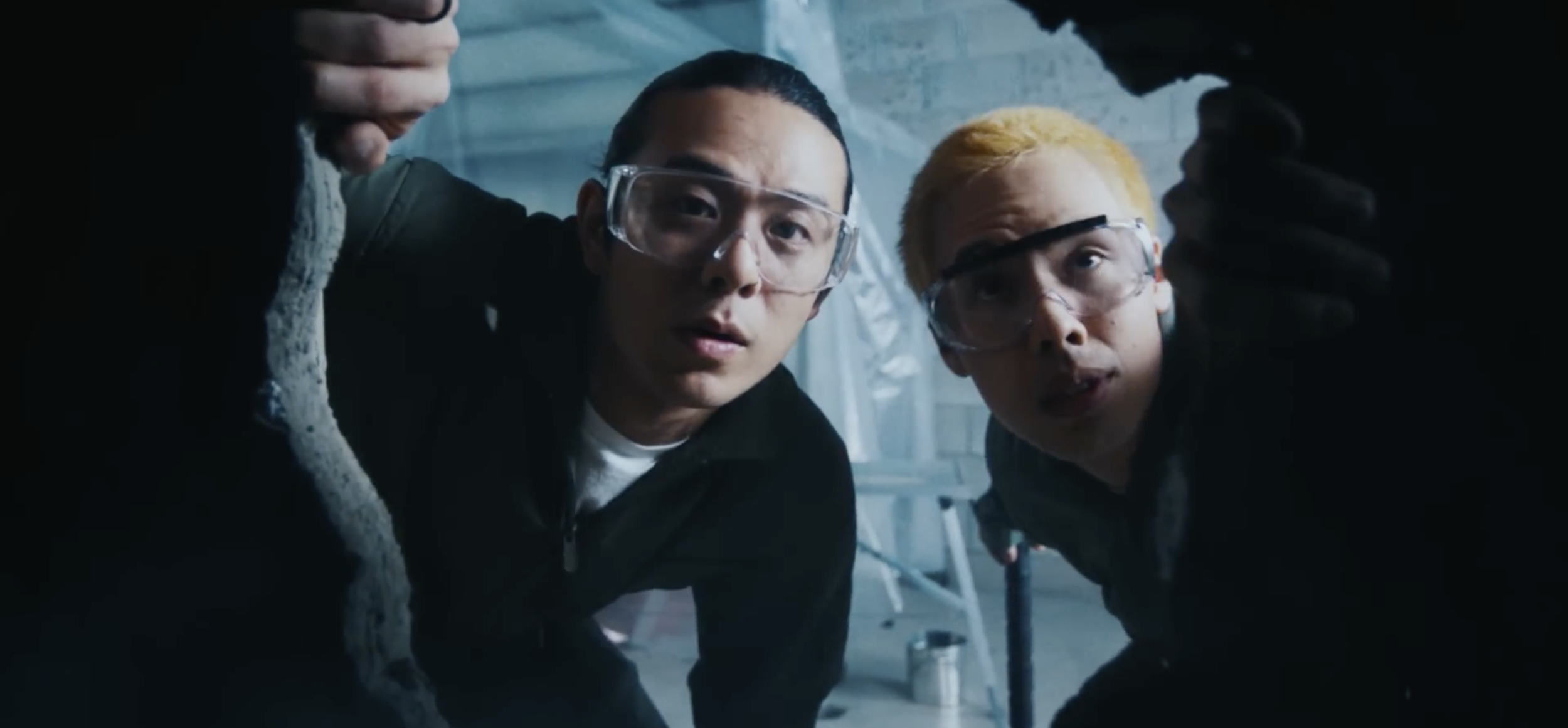 Deux personnes portant des lunettes de protection regardent à travers une ouverture, dans un environnement industriel ou de laboratoire.