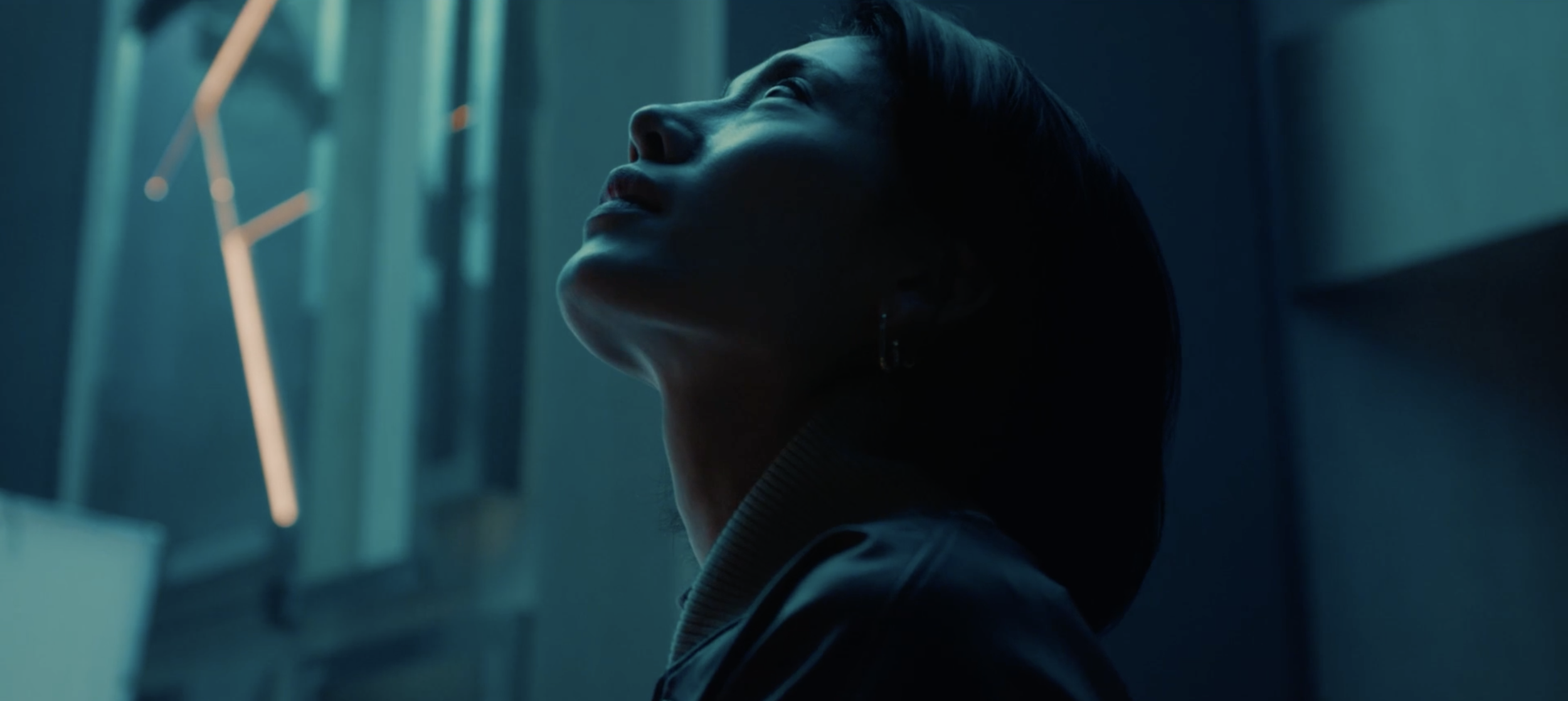 Personne regardant vers le haut, éclairée par une lumière bleue, dans un décor sombre.