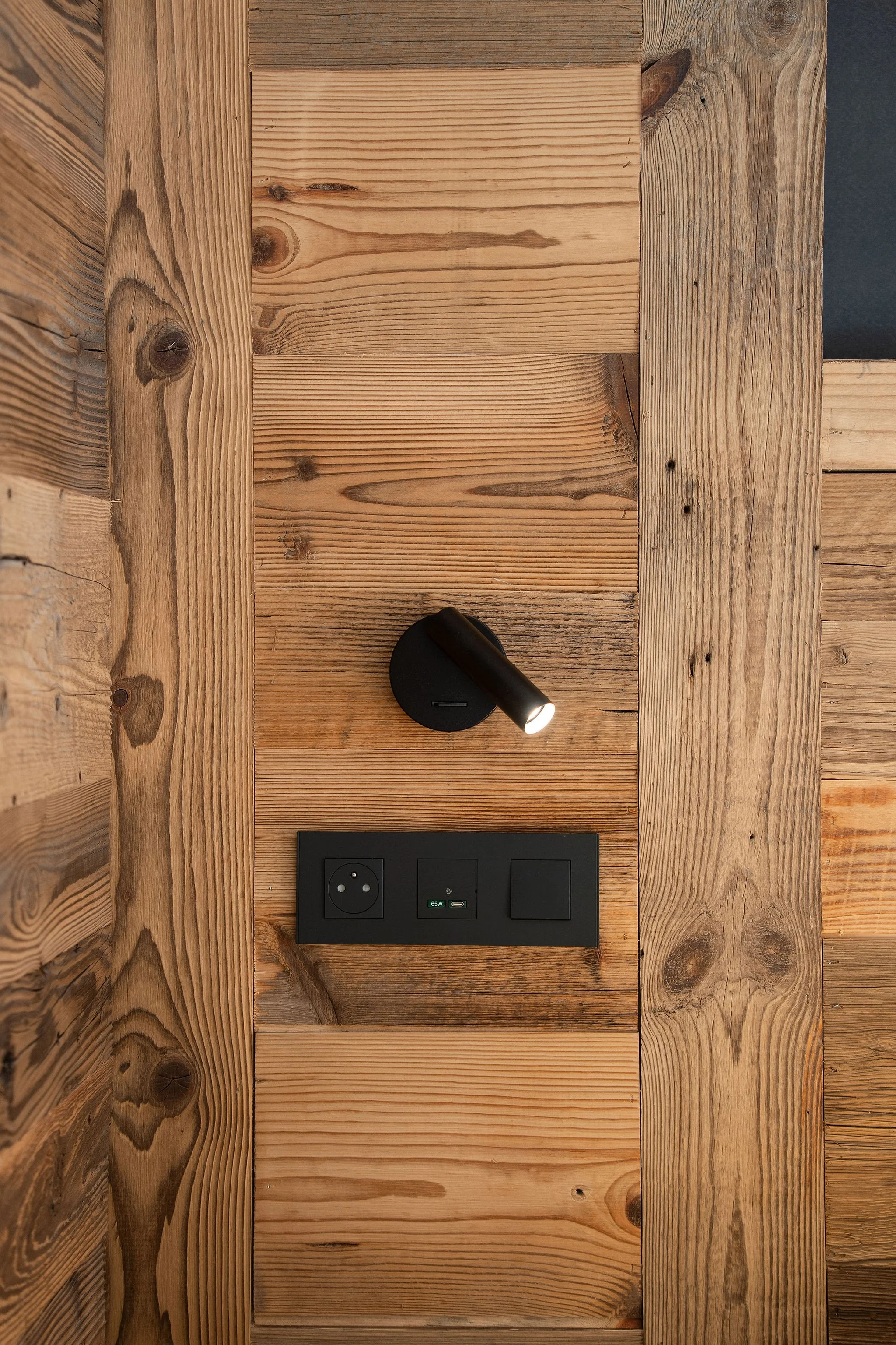 Surface en bois avec une prise électrique, un port USB, et un interrupteur, éclairée par une lampe directionnelle noire.