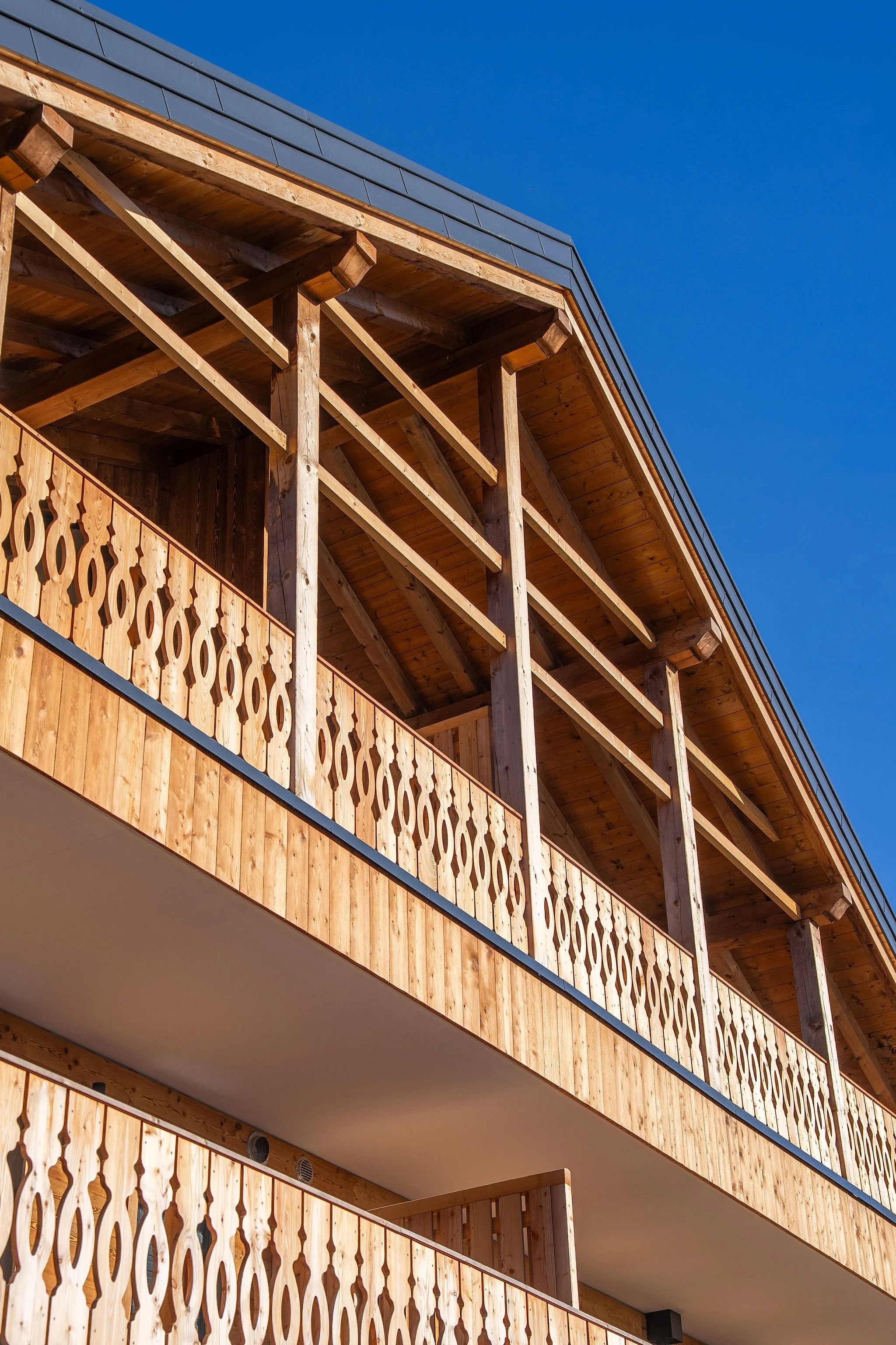 Façade d'un bâtiment en bois avec balcons en bois sculpté sous un ciel bleu clair.
