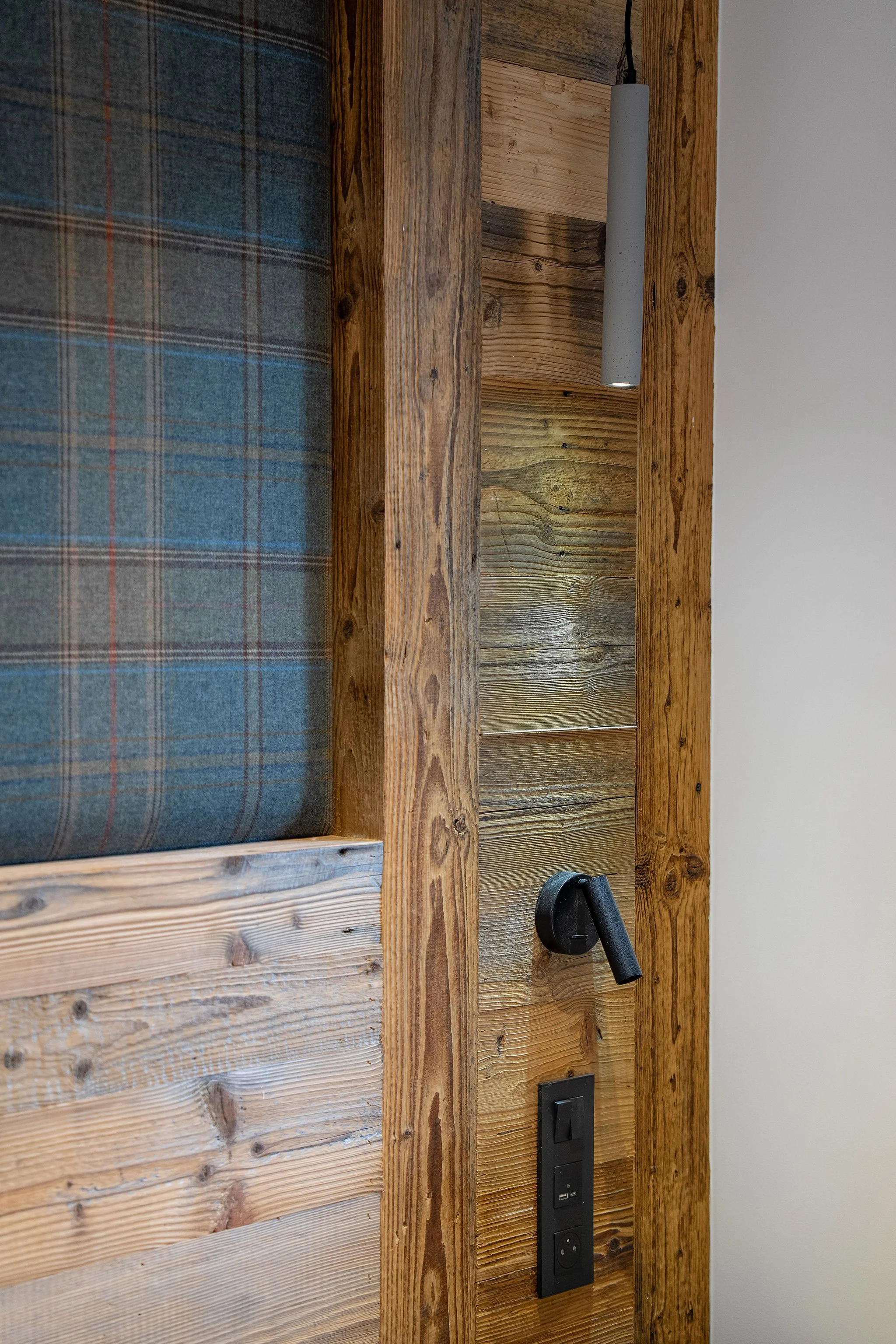 Prise électrique, interrupteur, support pour téléphone ou appareil électrique, et lampe encastrée sur un mur en bois dans un intérieur rustique.