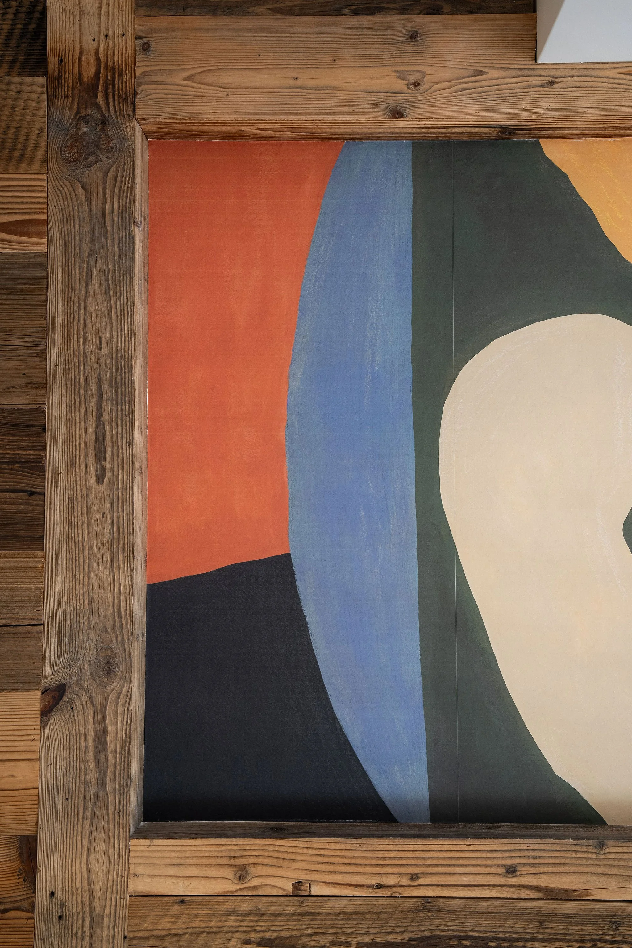 Peinture abstraite avec des formes colorées en rouge, bleu, vert, noir et blanc encadrée en bois en tête de lit d'un appartement de stryle chalet.