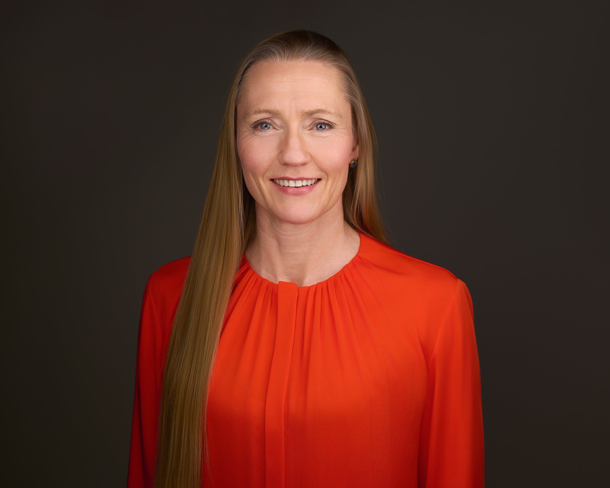 Ai-business-strategist-and-keynote-speaker-elin-hauge-wearing-an-orange-blowse-and-looking-at-the-camera.