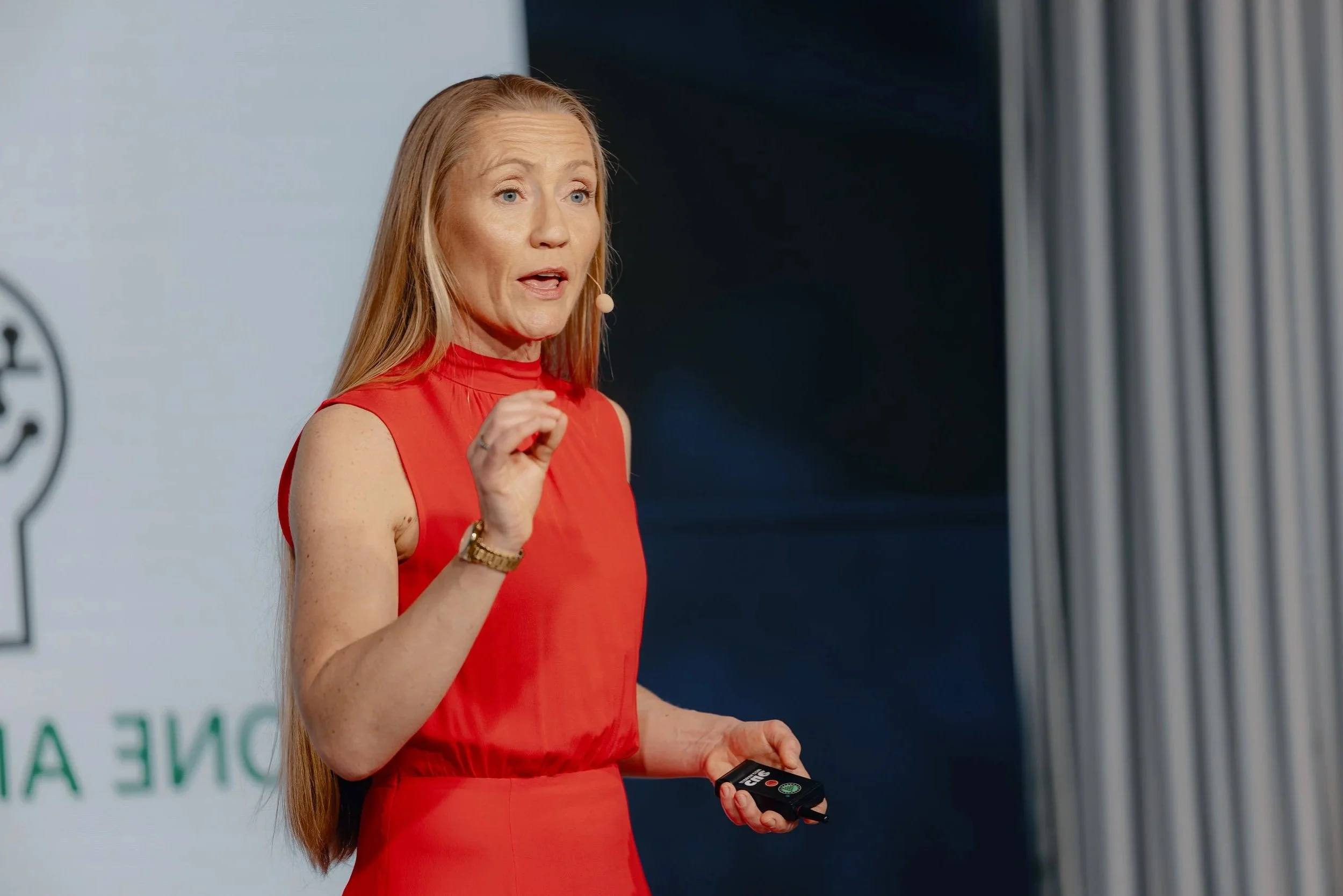Elin Hauge, Data and AI keynote speaker and strategist, speaking at a conference. Wearing an orange dress, standing on a stage, and wearing a microphone.