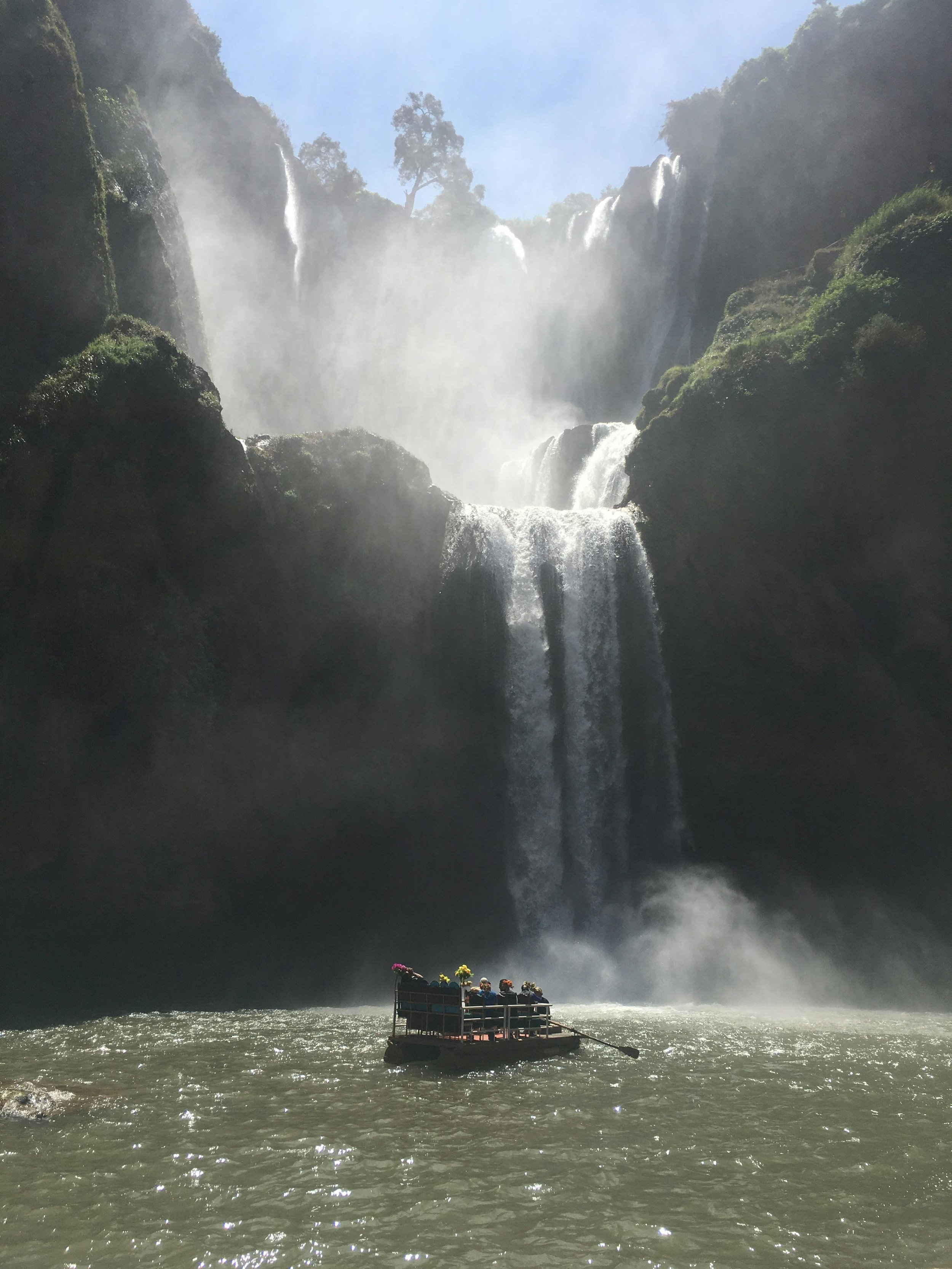 A group of people on a small raft approaching a waterfall with lush greenery surrounding it.