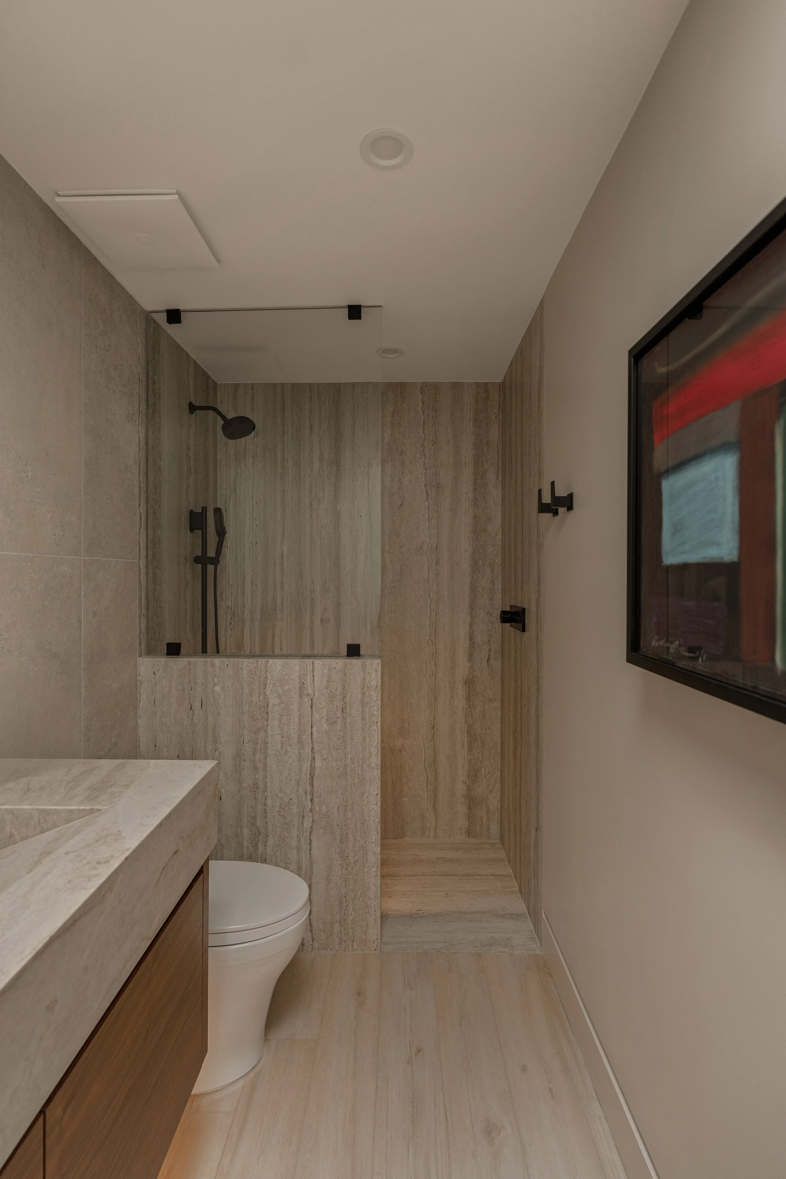 Detail of the modern rainfall fixture paired with warm, natural stone textures.