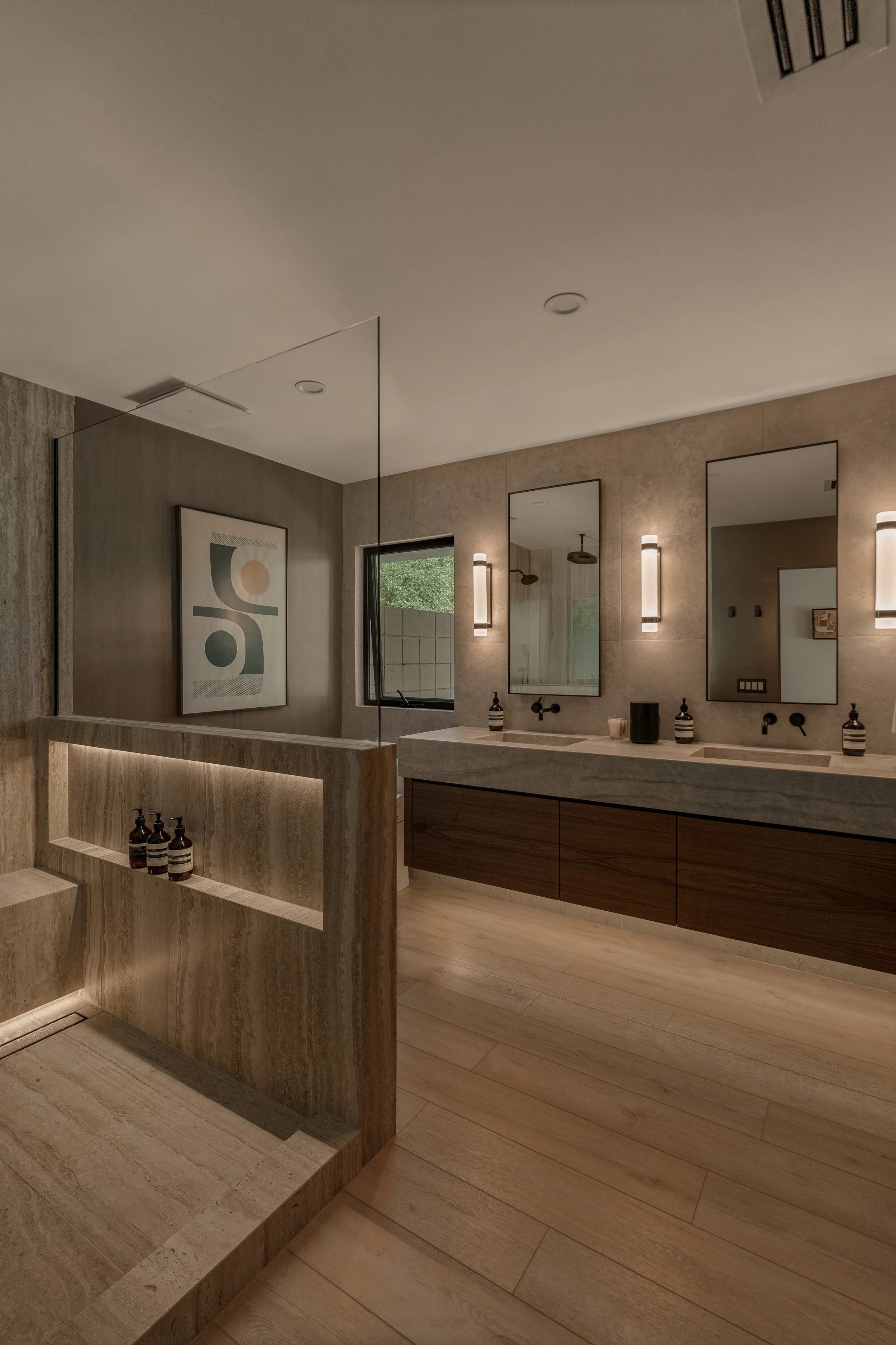 A wide view of the remodeled Palm Springs bathroom featuring a floating double vanity, warm stone finishes, and modern lighting designed by Symbol Design Studio.