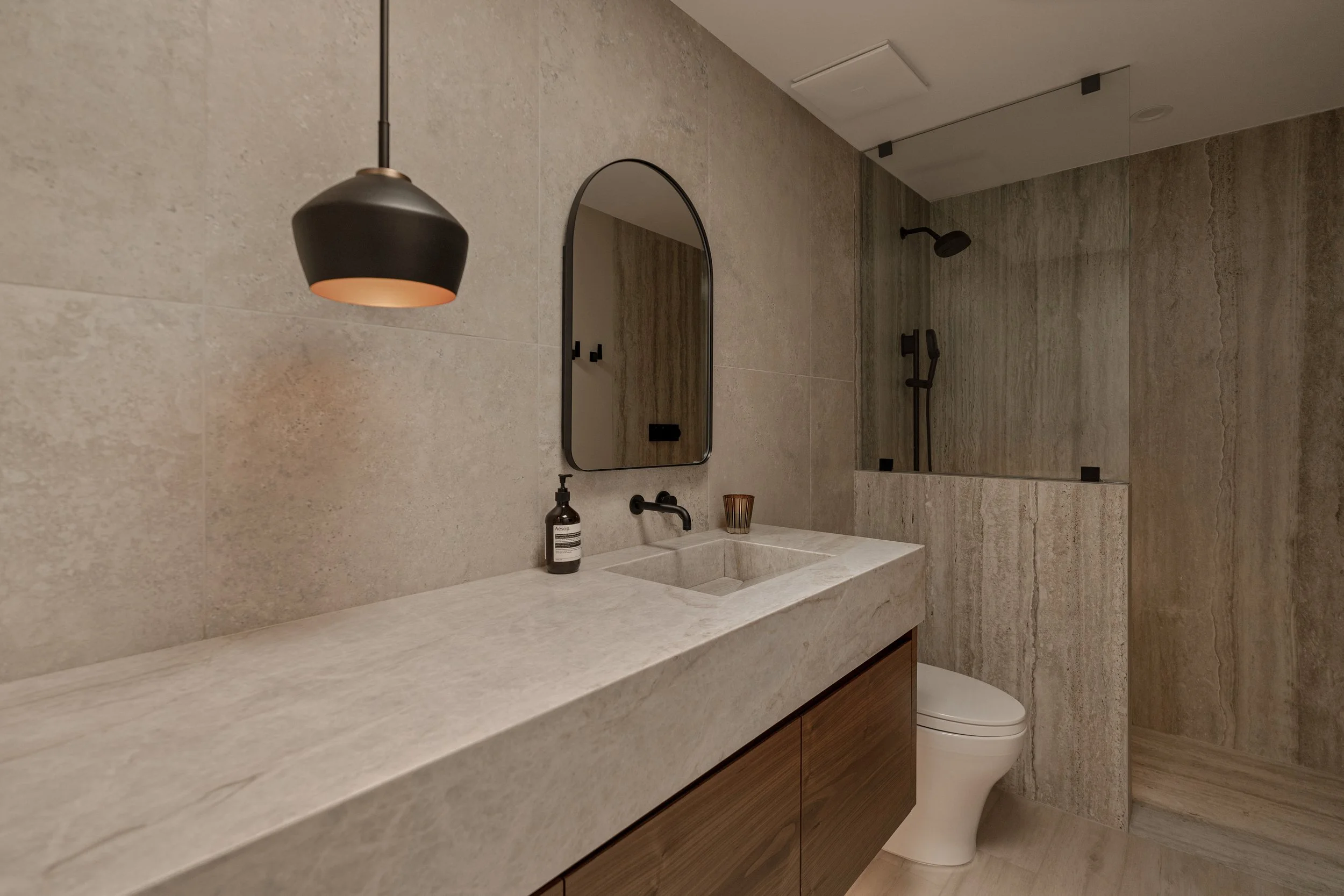 A refined view emphasizing the clean modern fixtures, vertical lighting, and handcrafted stone surfaces.