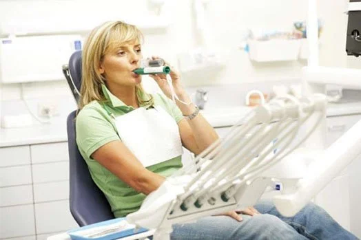 Woman sitting in a dental chair holding a breathing device in a dentist's office.