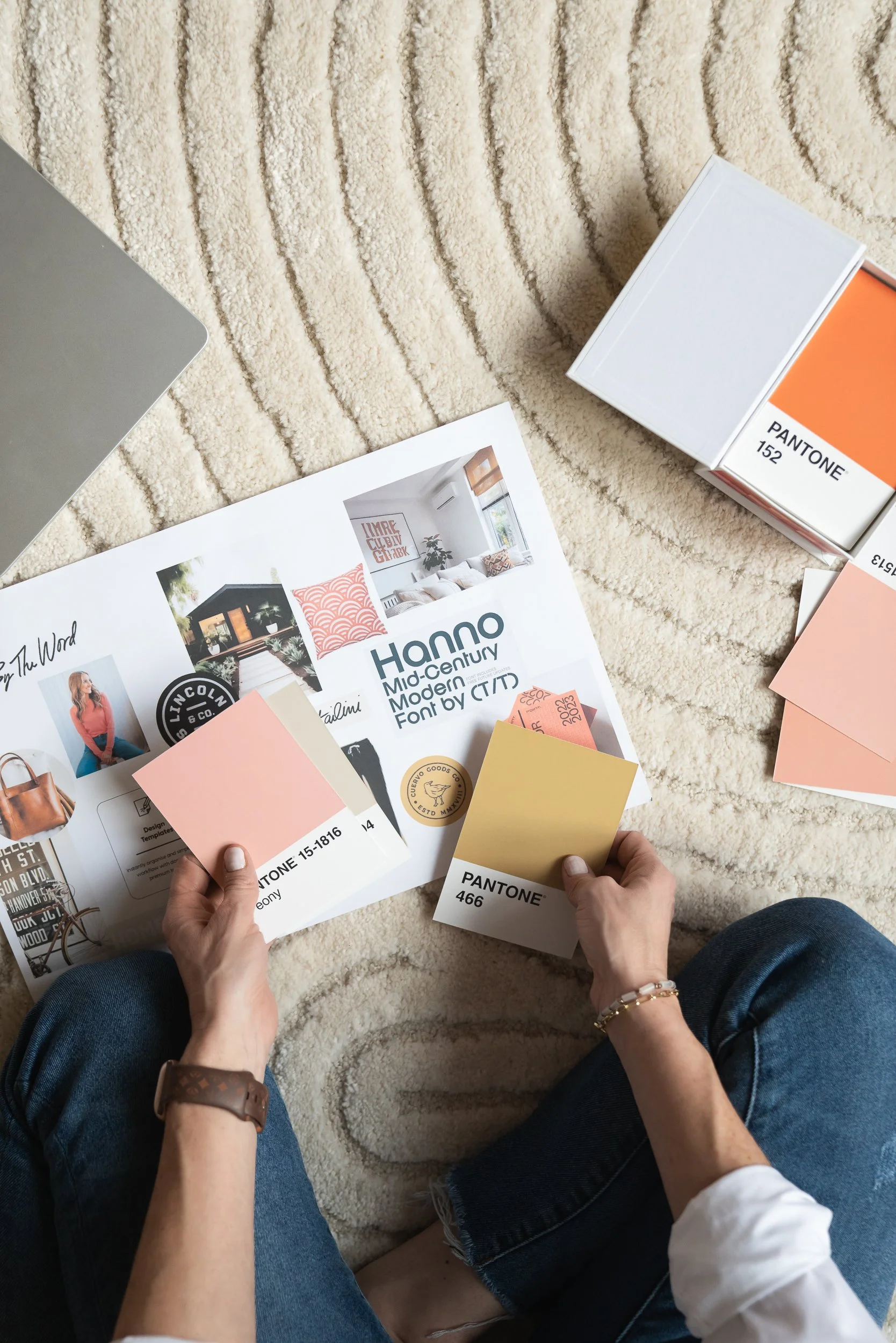Hands holding soft neutral Pantone color swatches over a brand mood board, showcasing a thoughtful color palette selection process for a creative brand identity.