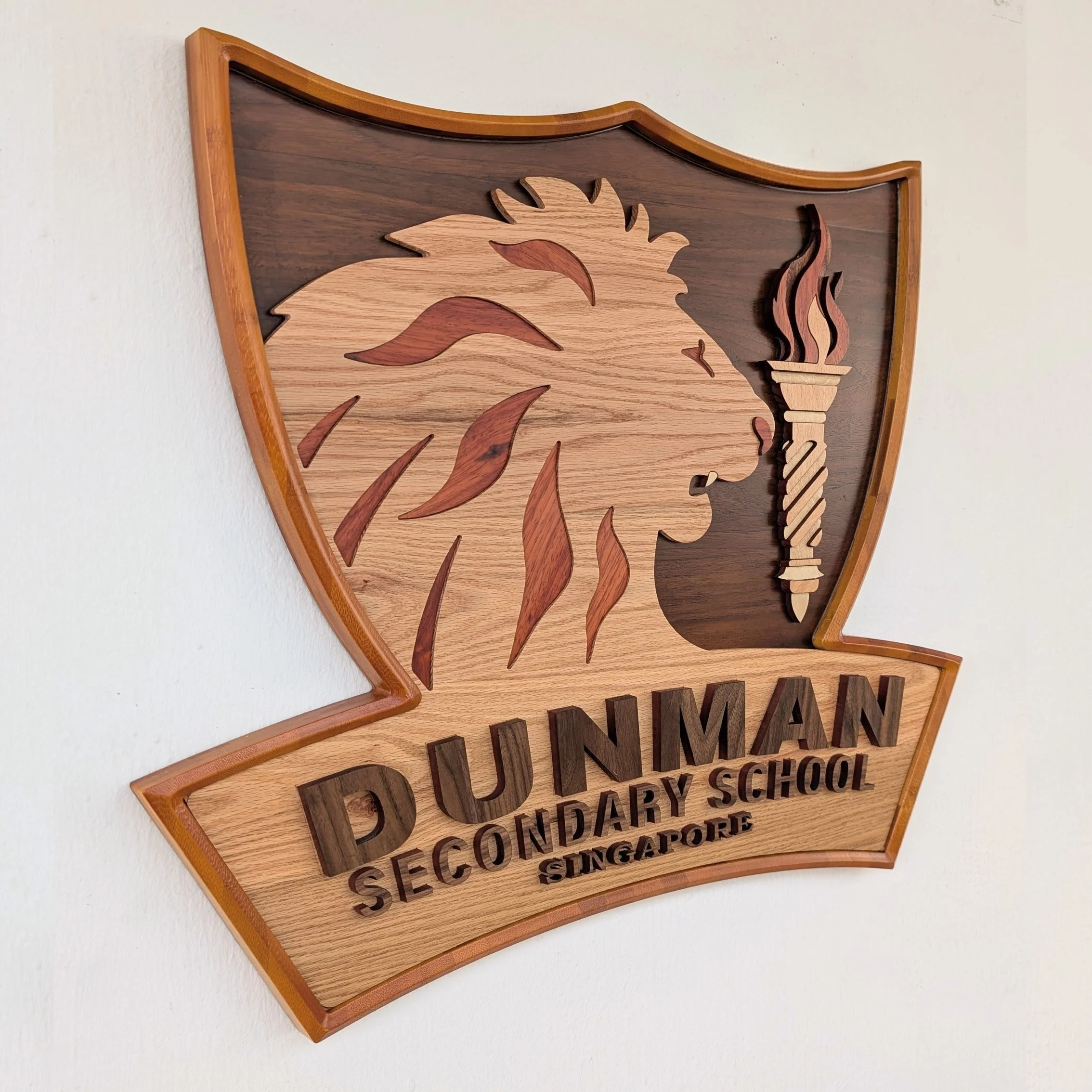 Layered hardwood wall sign for Dunman Secondary School featuring a lion silhouette, torch emblem, and precision CNC-cut timber construction.