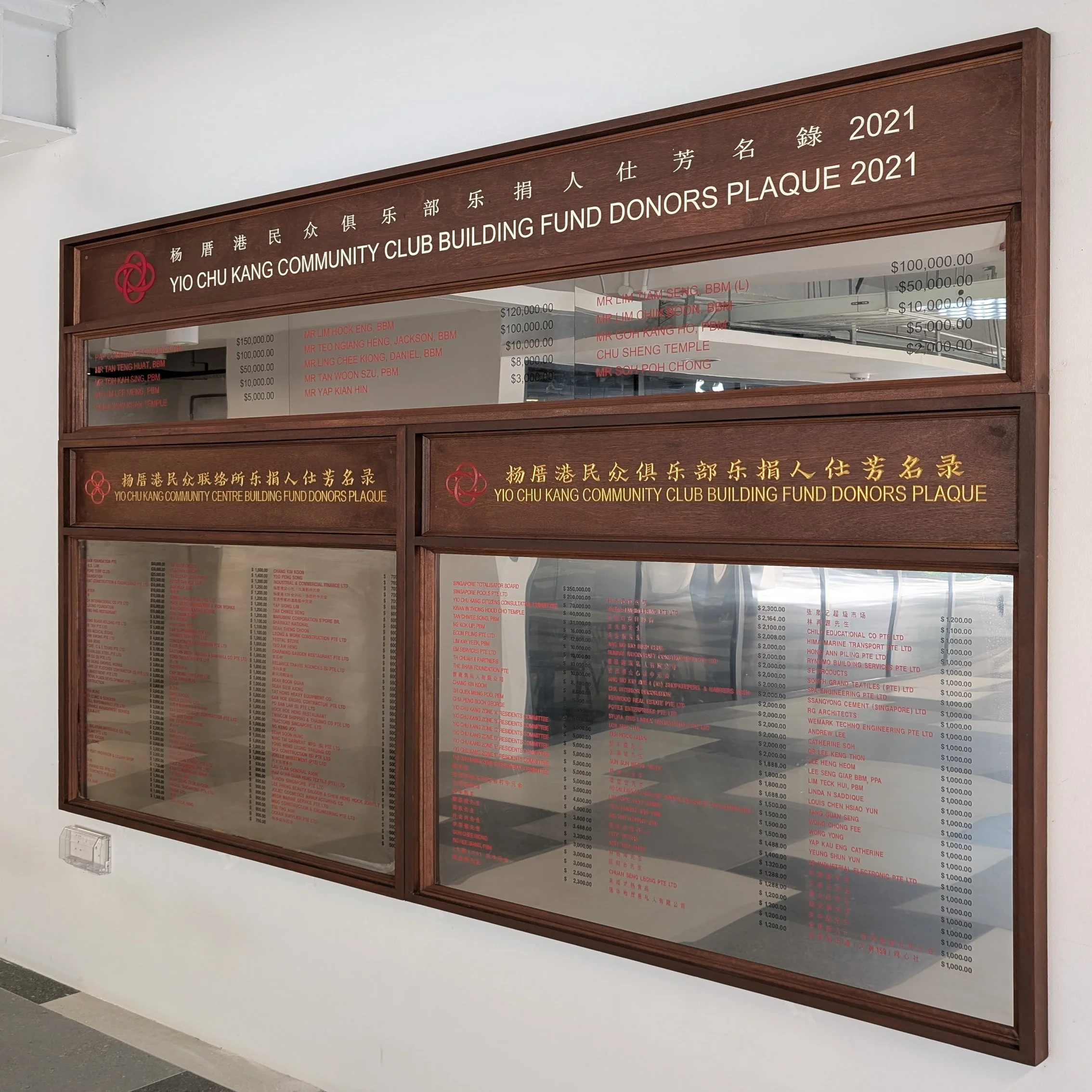 Large timber-framed donor recognition display with engraved bilingual headings, etched stainless steel panels, and premium wood finish for a Yio Chu Kang Community Centre.
