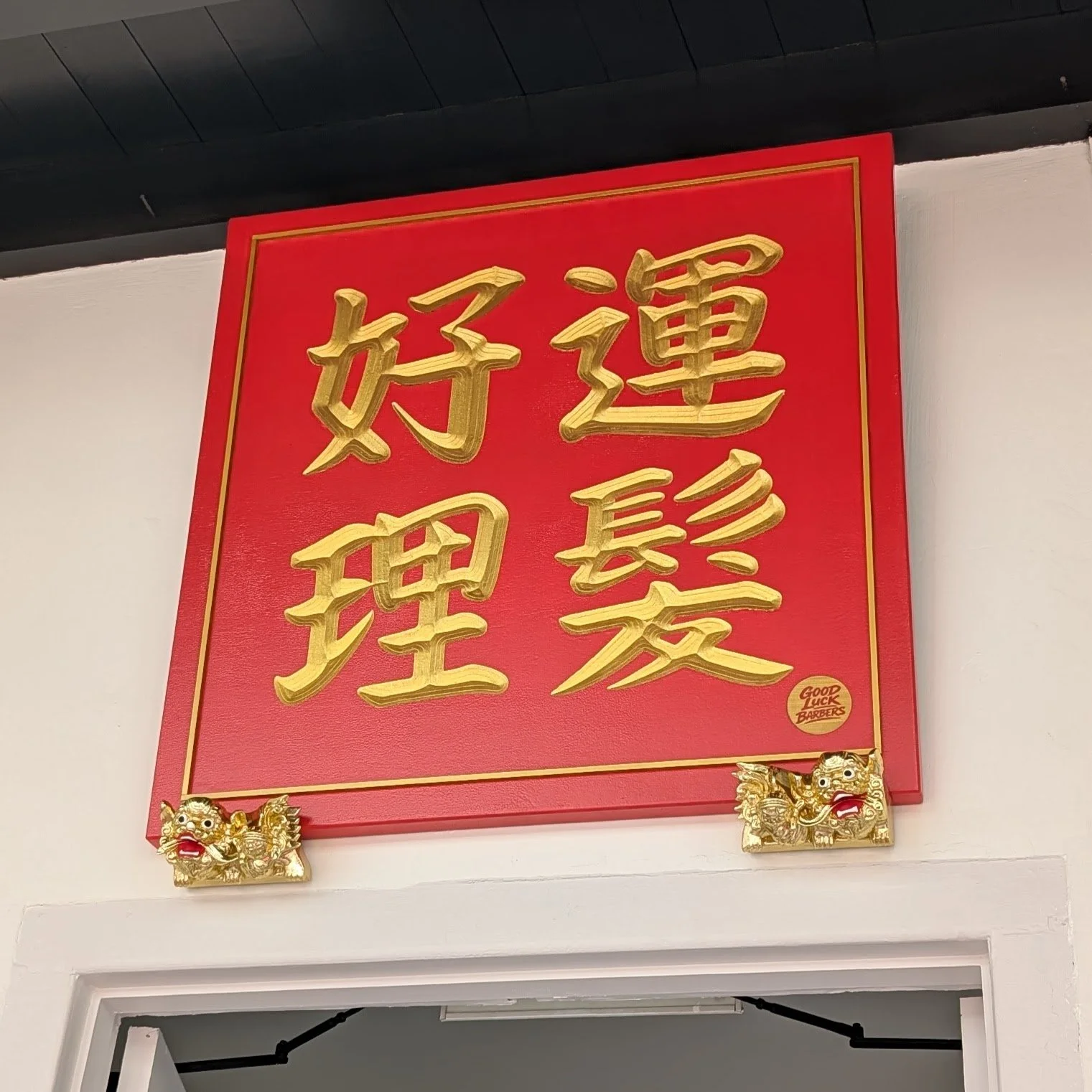 Custom handcrafted wooden barber shop sign with gold Chinese calligraphy, red lacquer finish, and traditional guardian lion ornaments for a barbershop entrance.