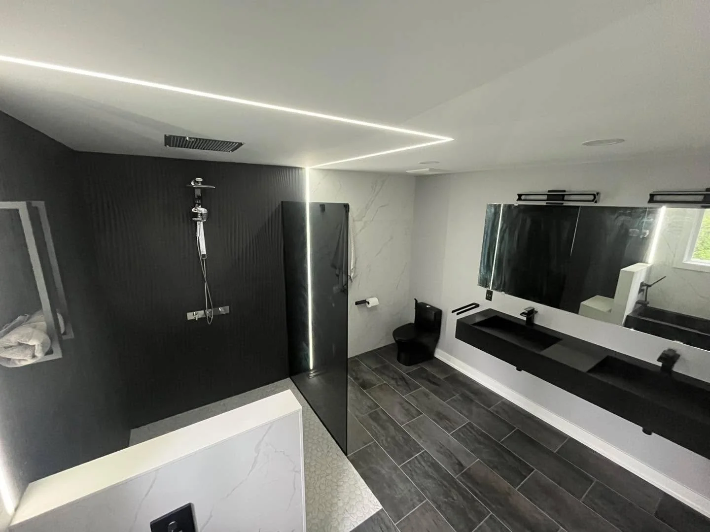 Black. White. Bold.
This custom bathroom renovation was all about modern contrast and clean lines &mdash; from the matte black fixtures and floating vanity to the LED accents and oversized tile work.

Designed to feel sleek, functional, and timeless.