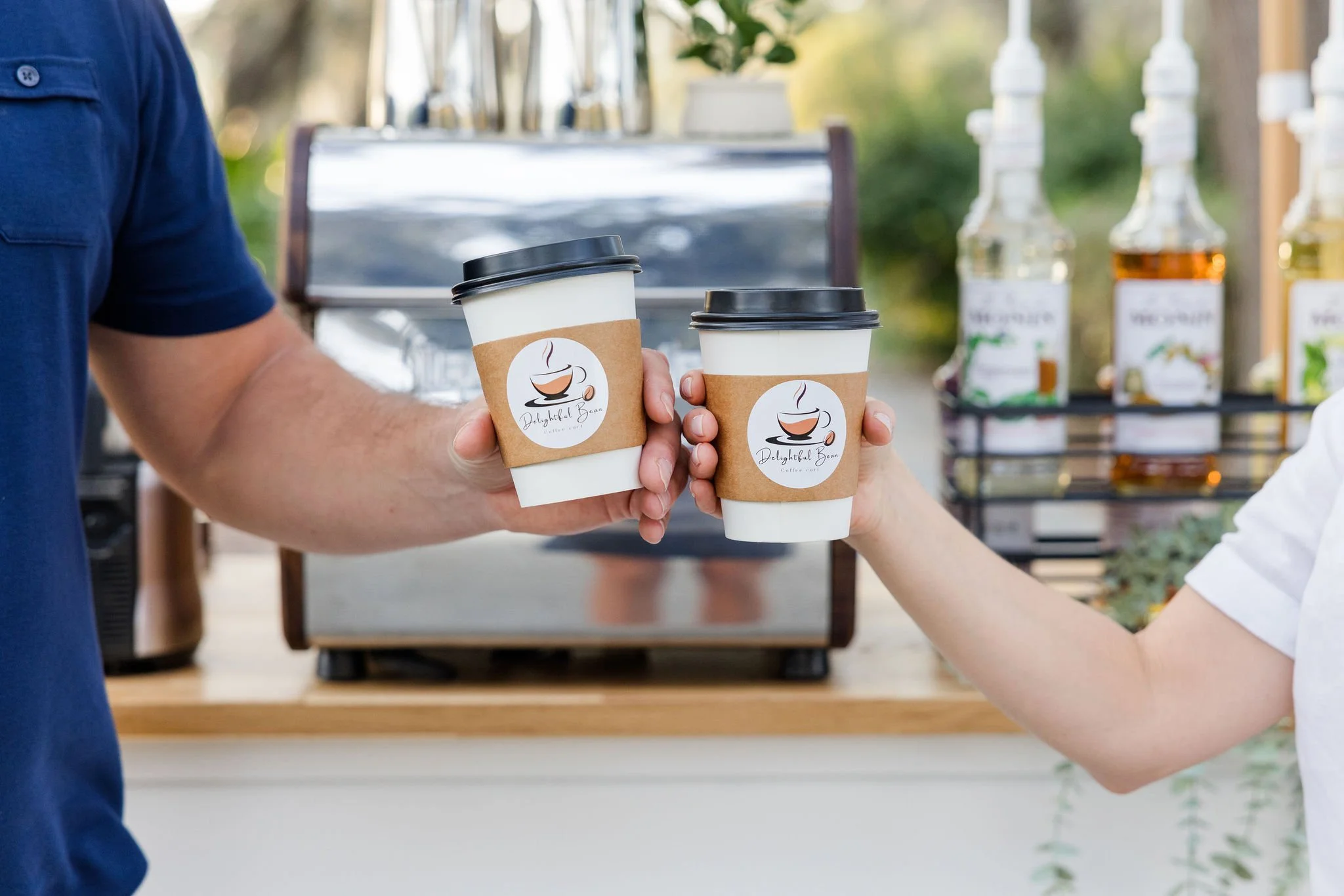 Two people holding coffee cups in front of a coffee machine; cups have "Delightful Beans" logo.