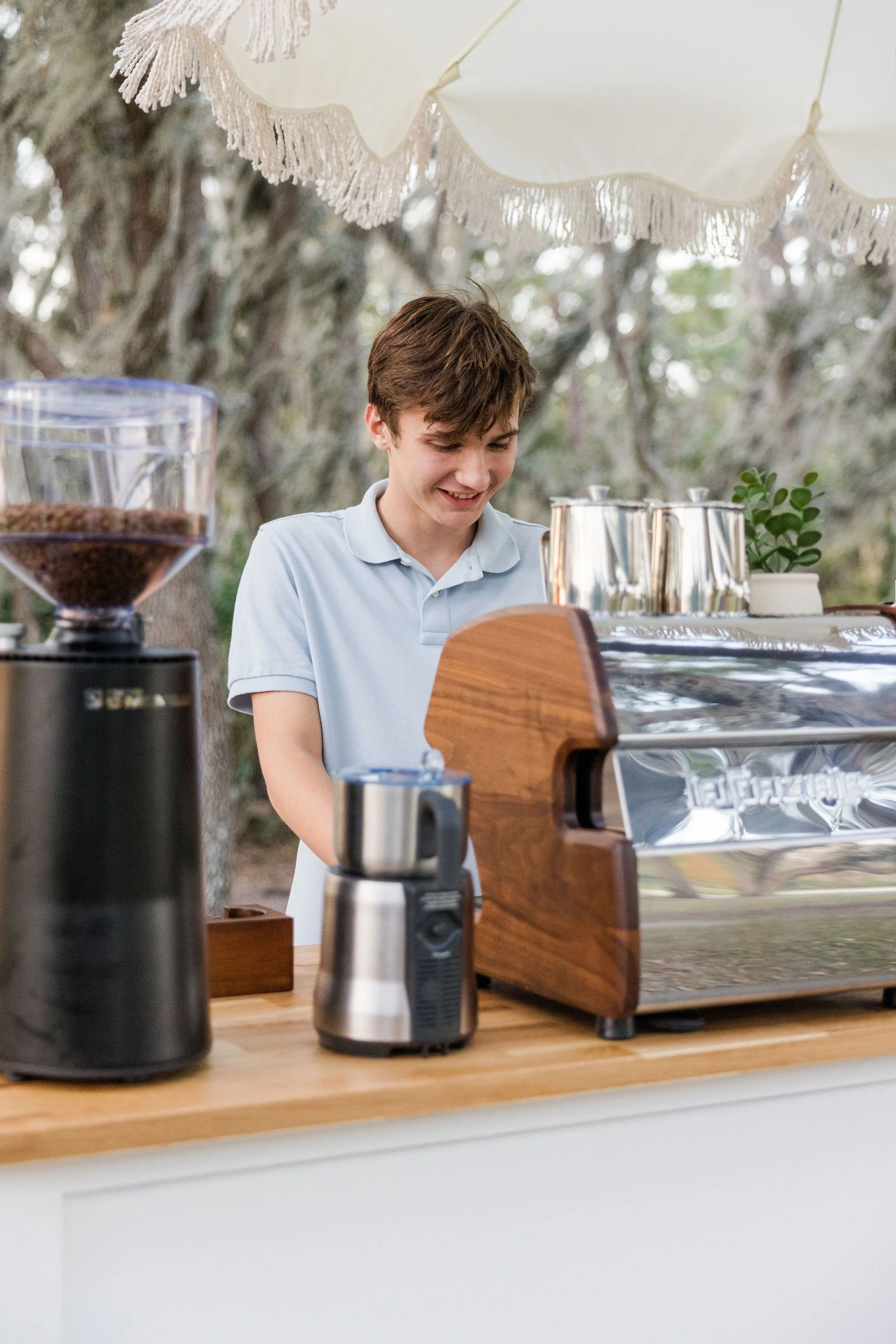 Young barista at outdoor coffee stand with espresso machine and grinder.