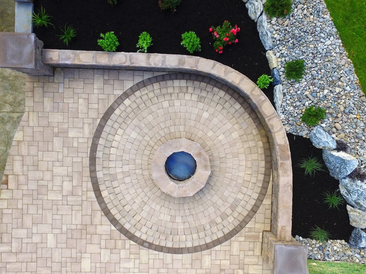 Backyard with white pergola, wooden deck, and patio; house in the background, grass and wooden fence surrounding the area.