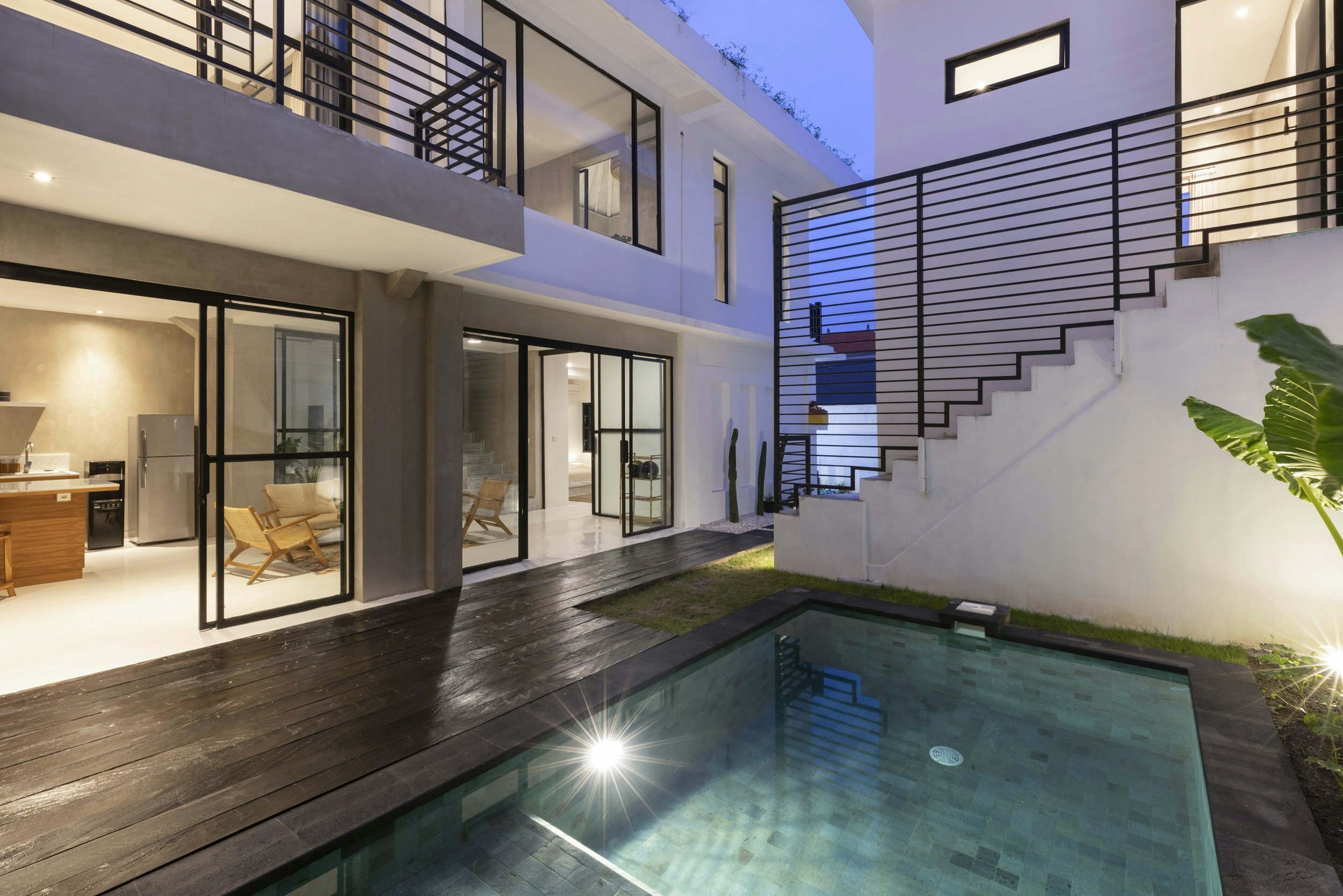 Modern home exterior with pool, large windows, and staircase at dusk