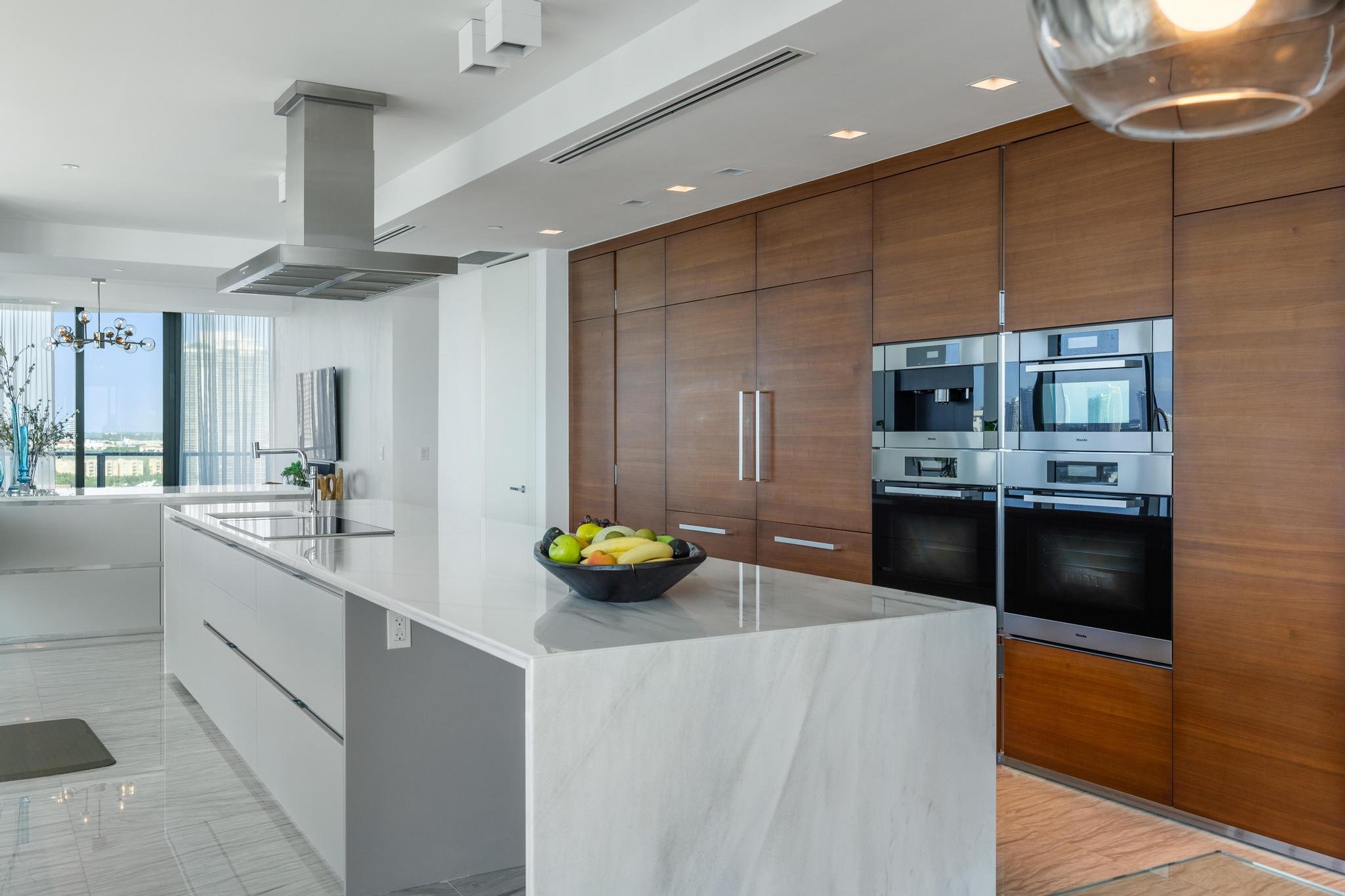 Modern kitchen with marble island, stainless steel appliances, wood cabinets, and fruit bowl.