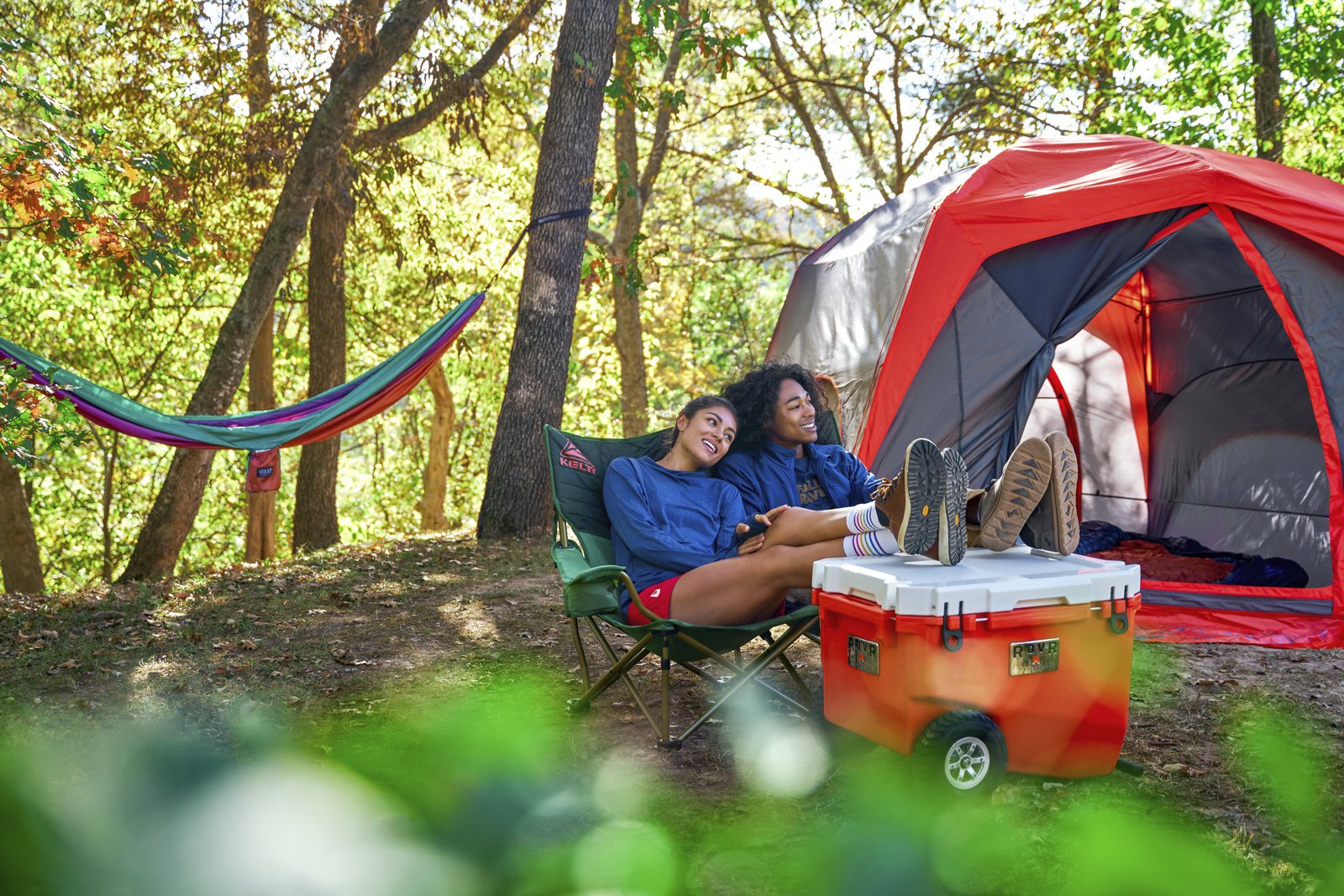 Couple Lounging at Camp Scene Sharing Kelty Loveseat RollR 60 Wheeled Cooler Big Agnes Big House Tent.