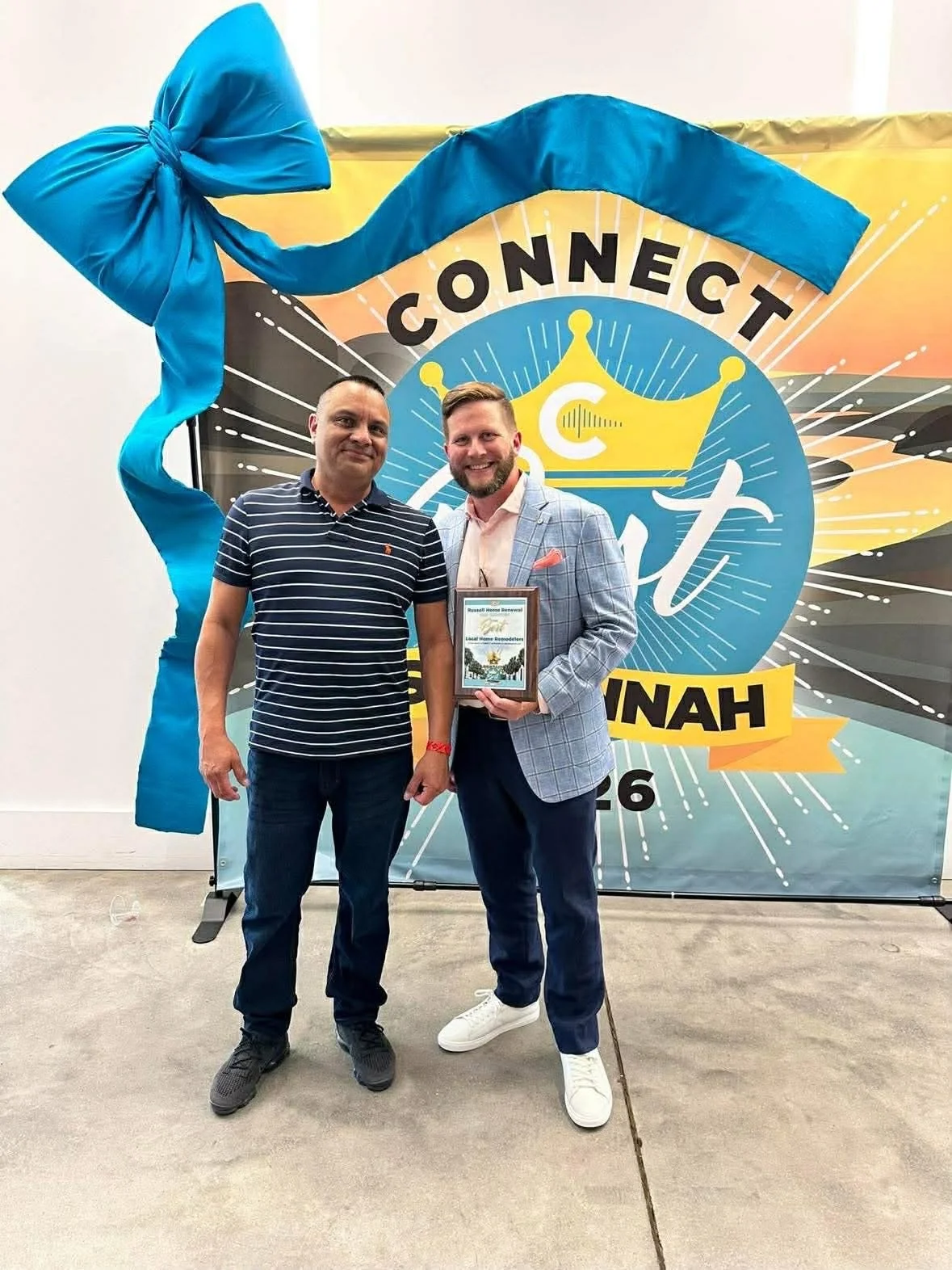Two men standing in front of a colorful banner that reads 'Connect U'', with one man holding a framed certificate and both smiling.