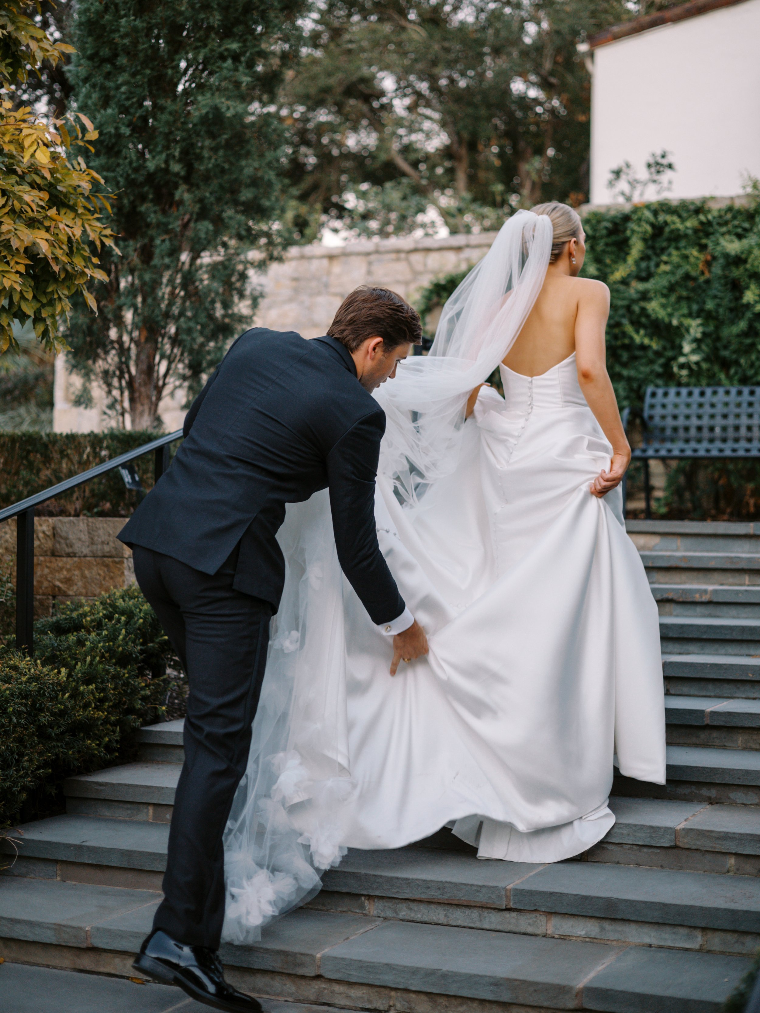 Groom helping bride with dress during newlywed photos at Dallas Arboretum wedding in Texas