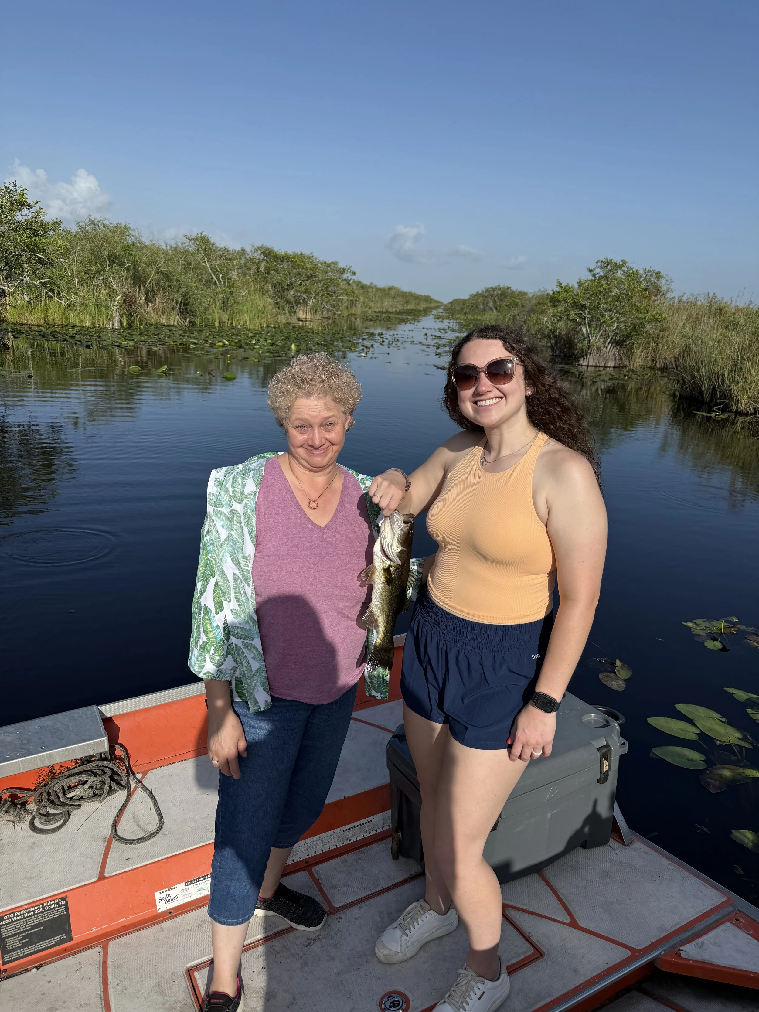 Two women holding a largemouth bass aboard a boat in the Everglades