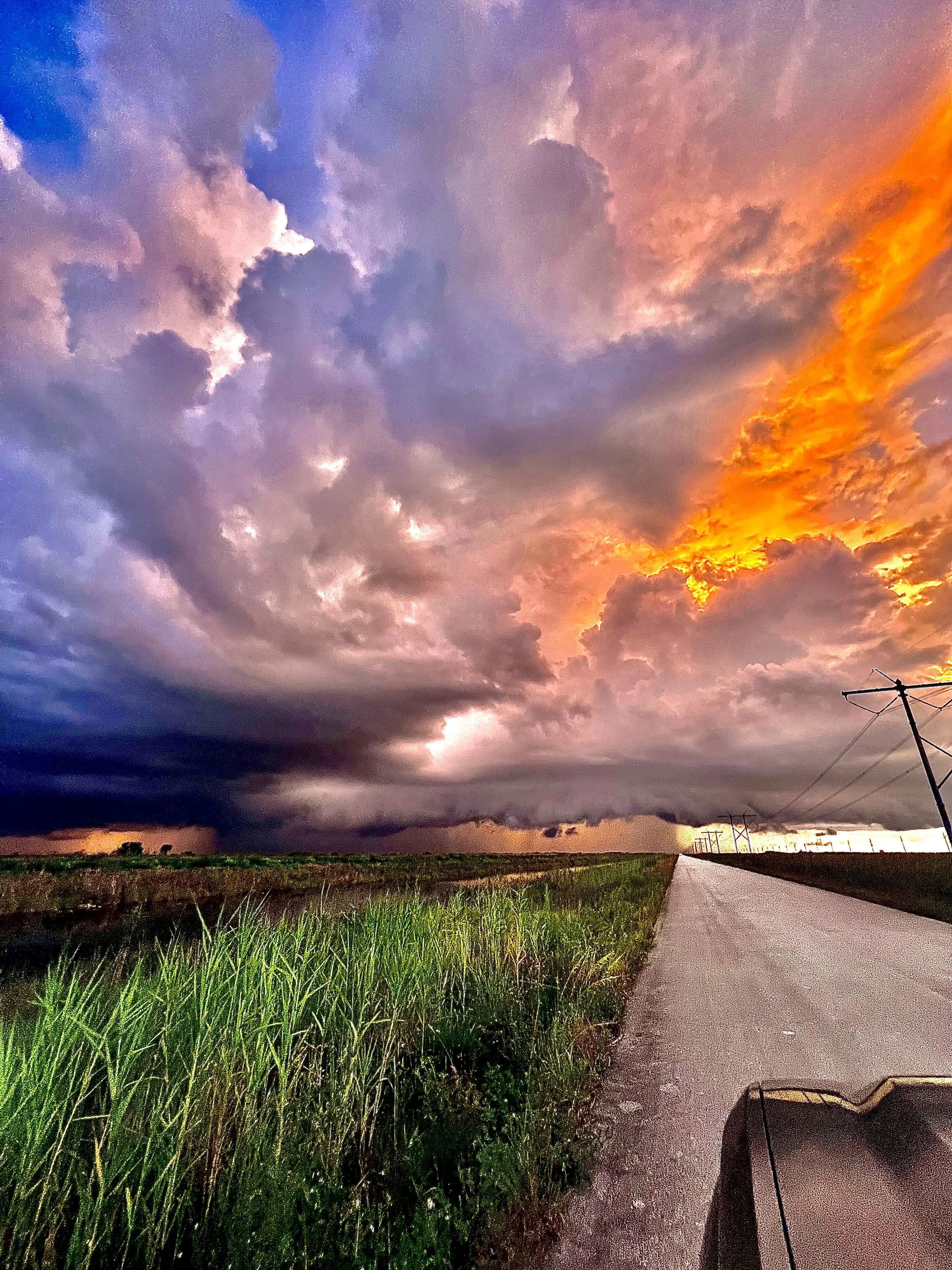 Road through open wetlands beneath dark clouds and an orange-pink sky