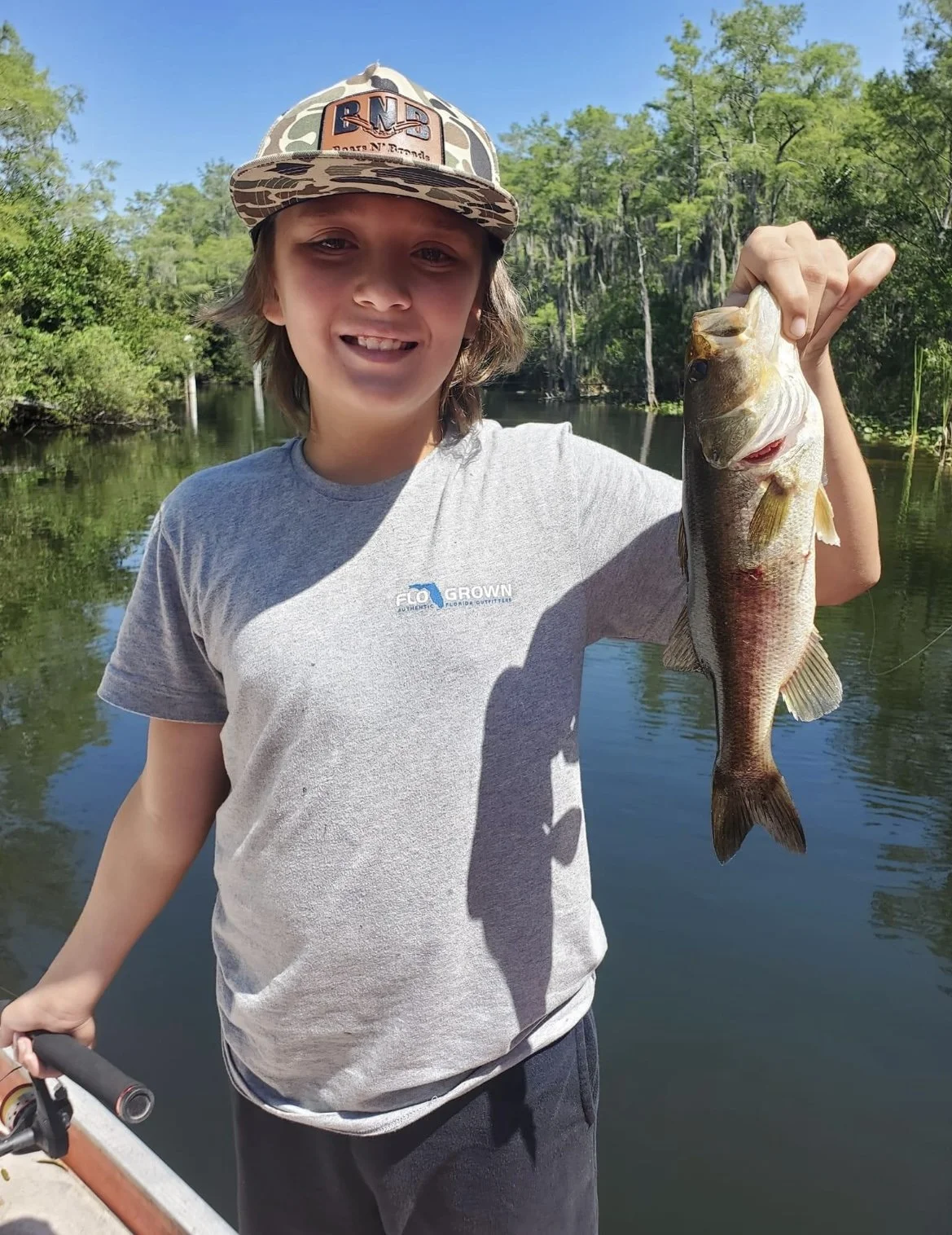 Young angler displaying a largemouth bass beside an Everglades waterway