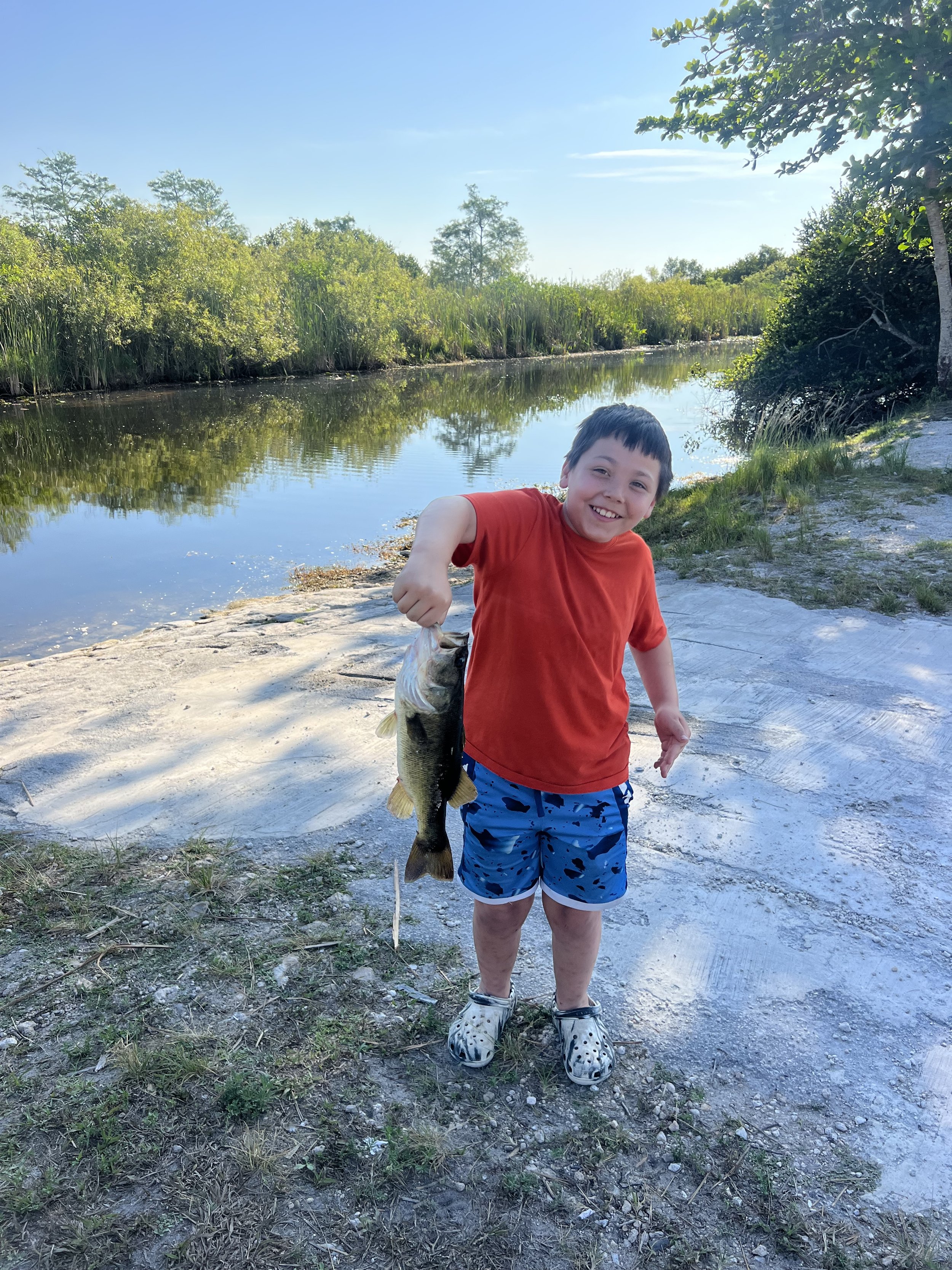 Boy in a red shirt holding his catch beside an airboat ramp
