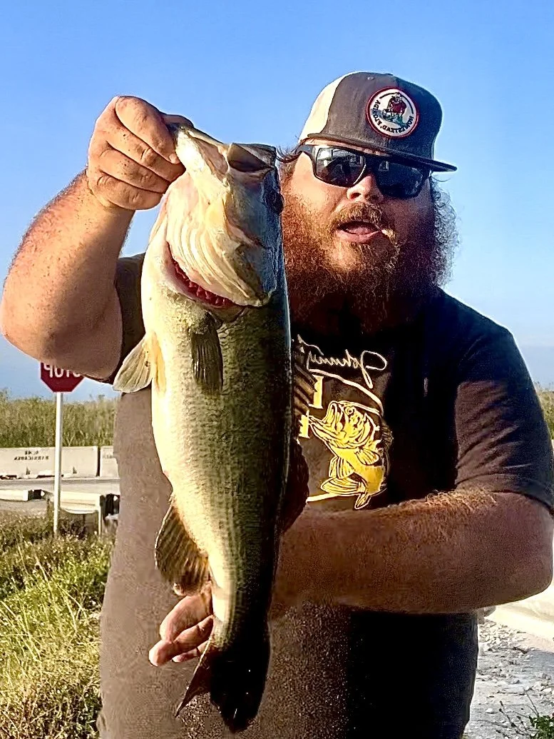 Angler wearing a cap and sunglasses holding a largemouth bass in the Everglades