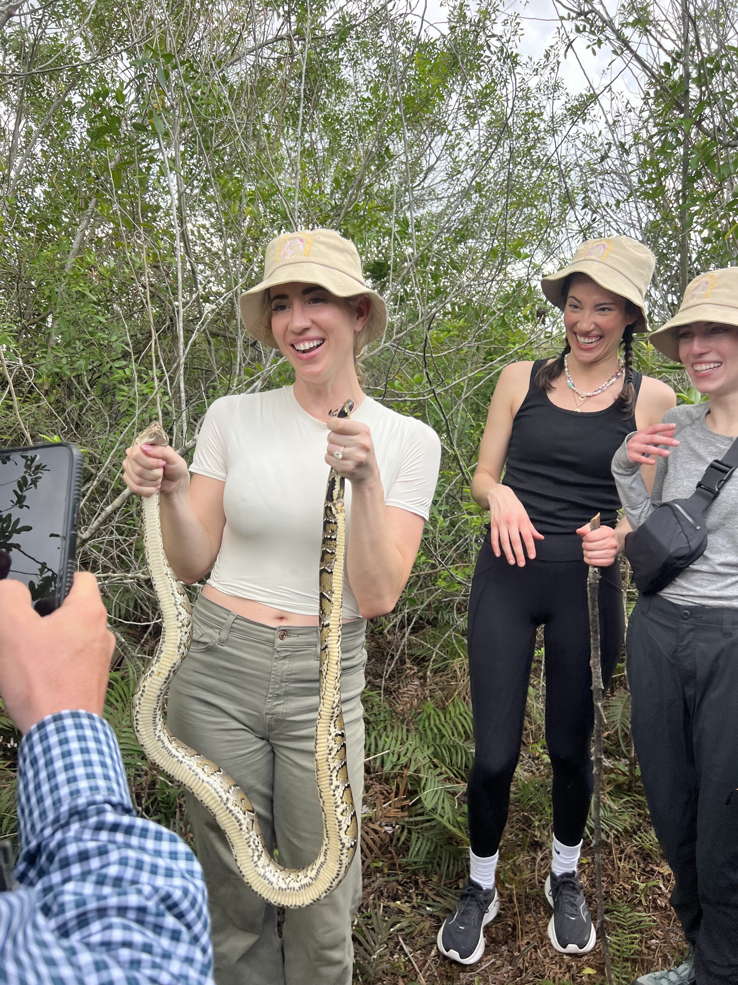 Guests in outdoor clothing holding a Burmese python in a wooded area