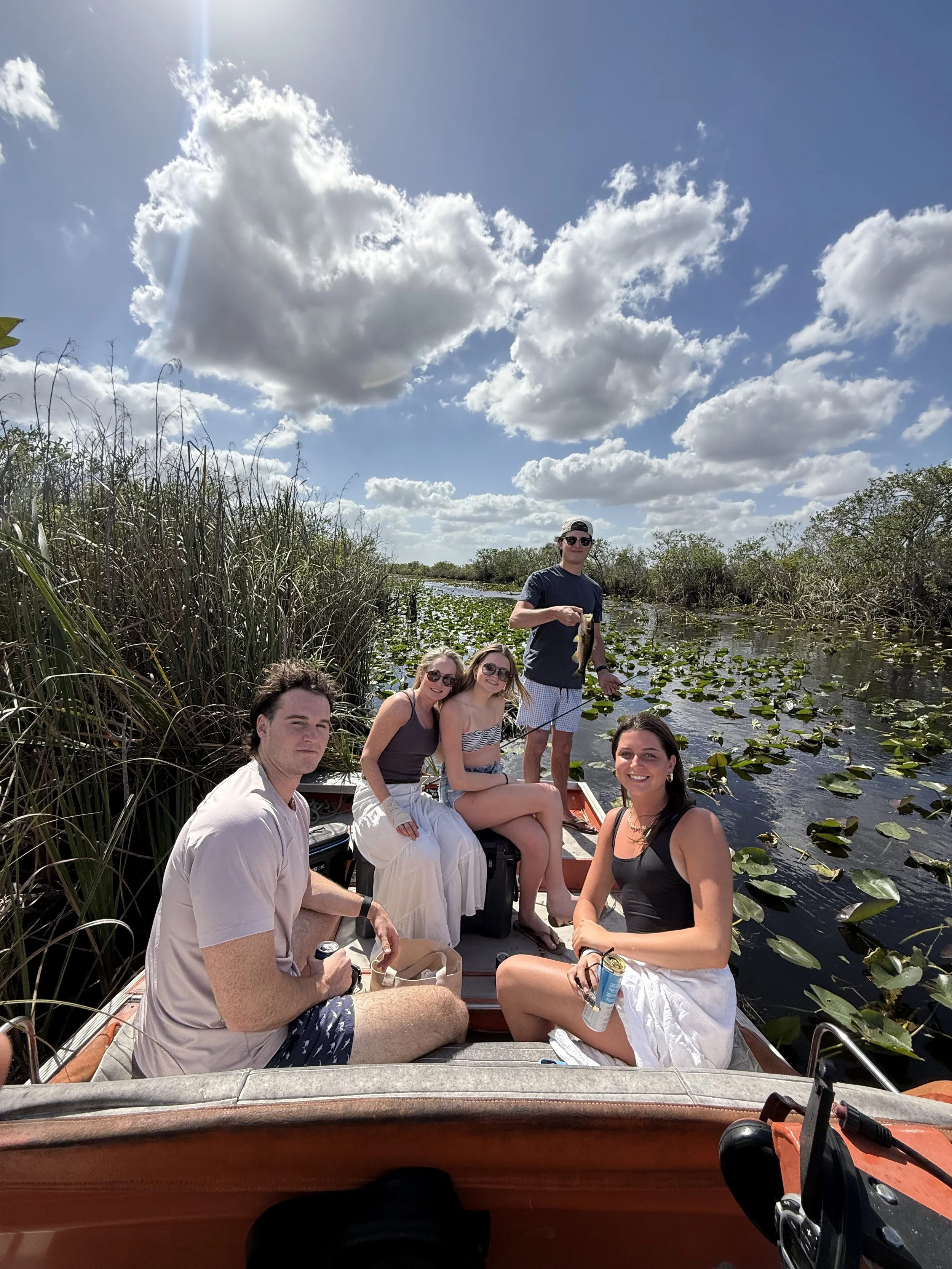 Group displaying their catch aboard an airboat among Everglades lily pads