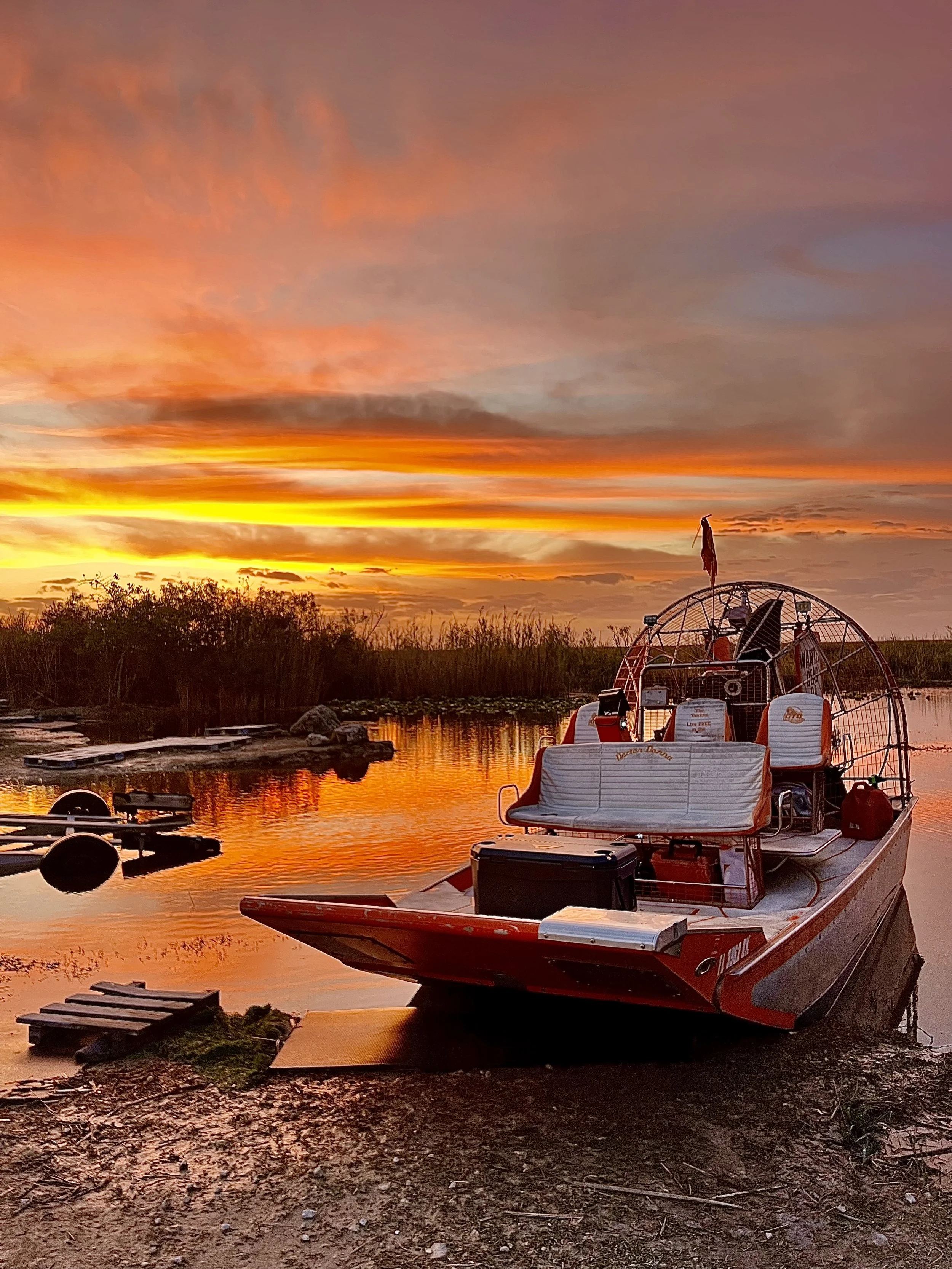 Airboat beside an Everglades waterway beneath an orange sunset