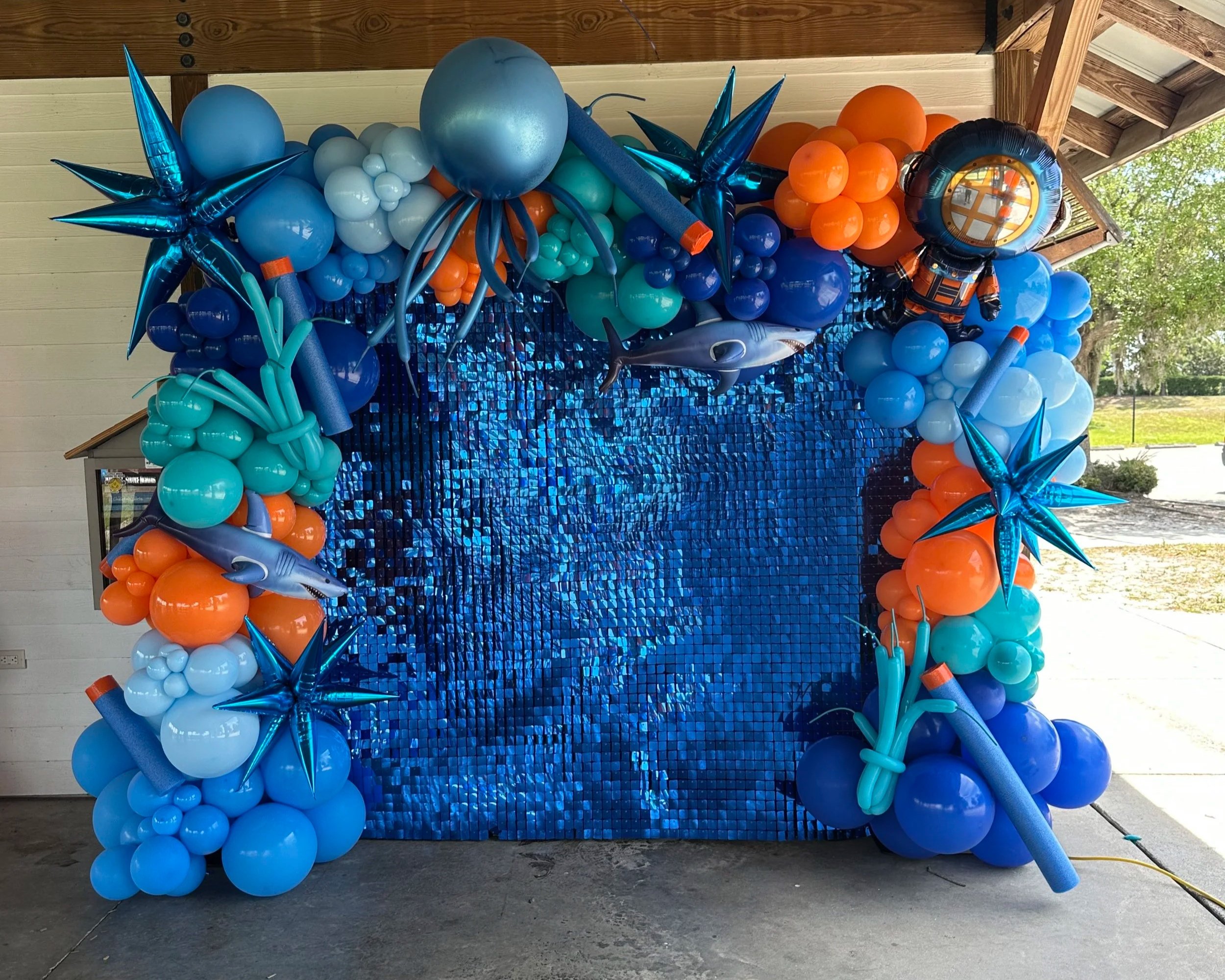 gamer birthday party backdrop, blue shimmer backdrop for a boy party, nerf gun party, shark balloons, blue starburst balloons, orange balloons, scuba diving balloon, outdoor birthday party in sarasota. Backdrop rental in sarasota, Lakewood Ranch.