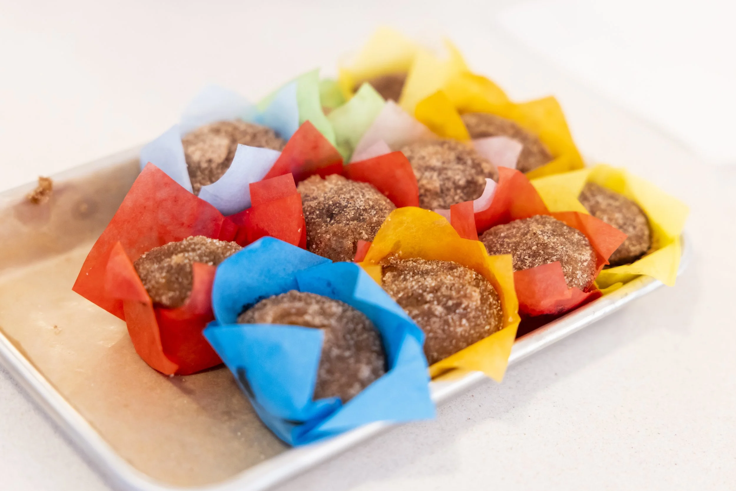 Assorted small brown cookies placed in colorful paper cups on a white tray.