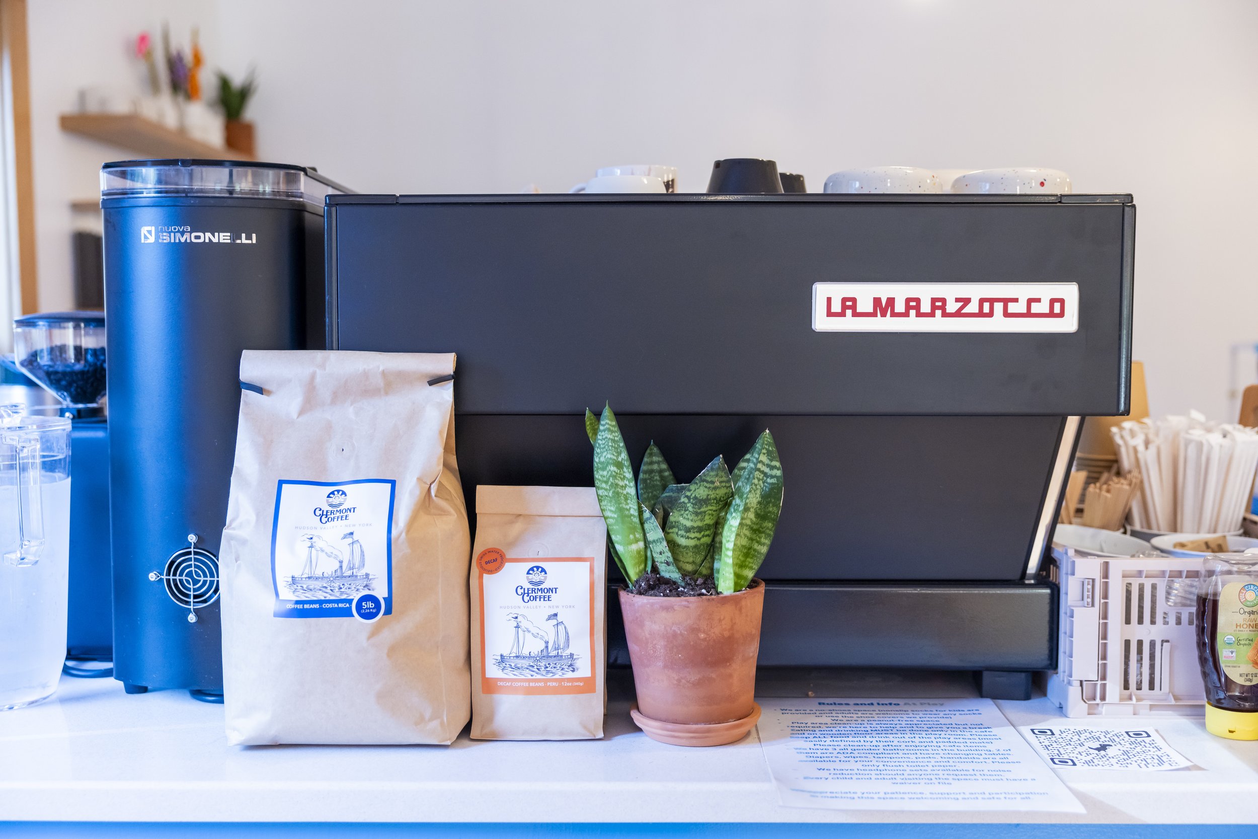 Coffee machine with bags of coffee beans, a potted plant, and coffee cups on top in a cafe setting.