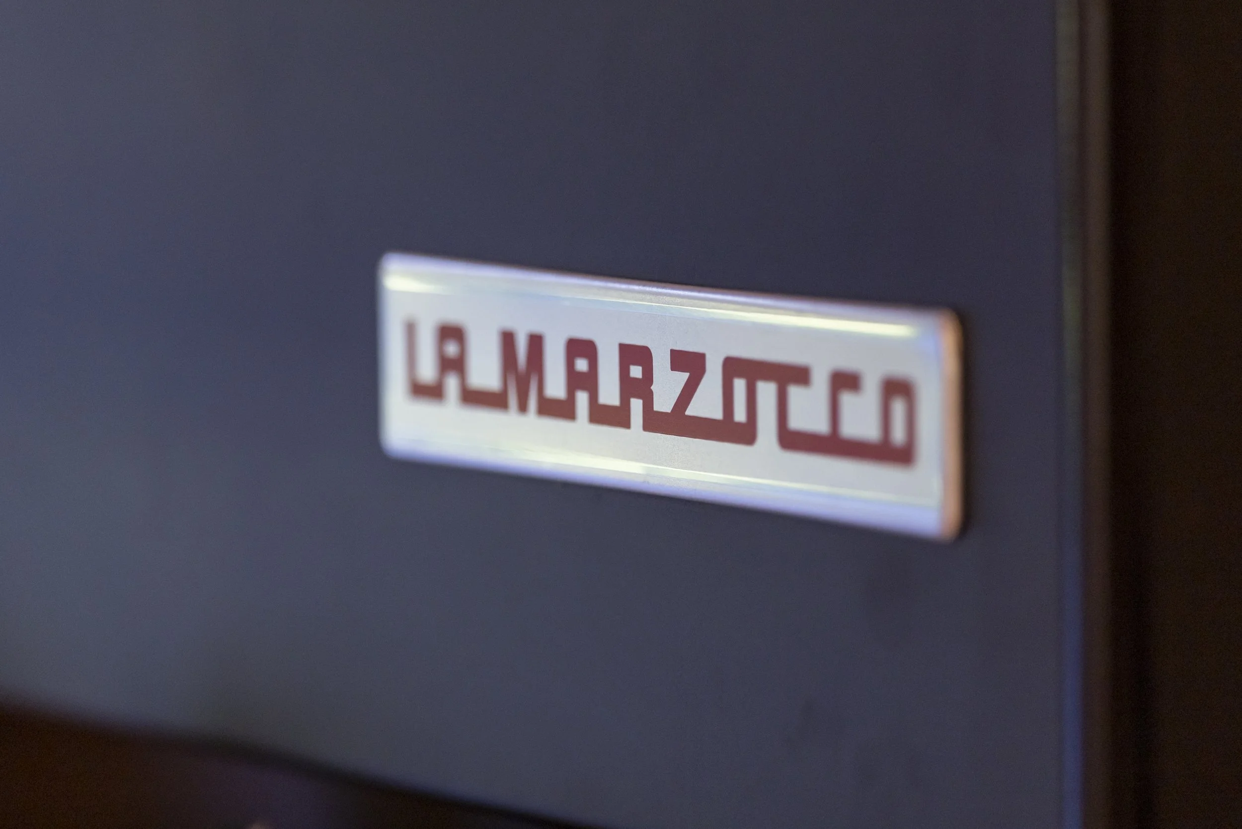 Close-up of a metallic label with red text reading 'LA MARRZOCA' on a dark surface.